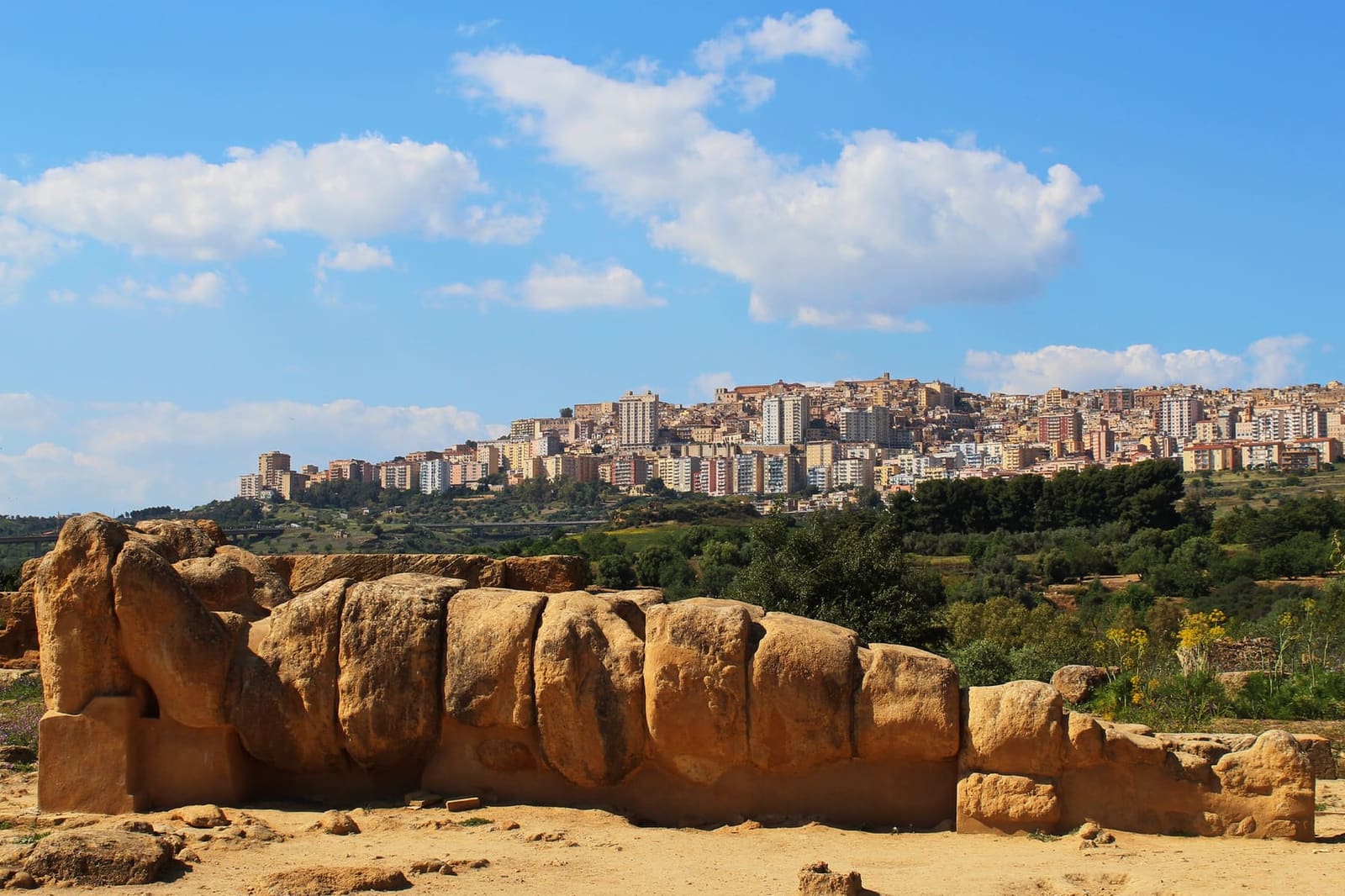 un telamone del tempio di Zeus Olimpio steso fra le rovine della valle, e sul colle, dietro, la città di oggi