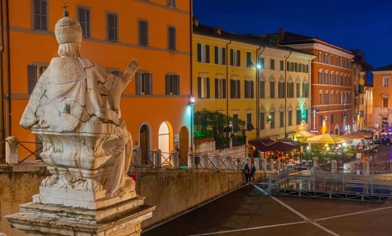 la statua di Clemente XII di spalle e la piazza del Papa illuminata, con i tavolini dei locali