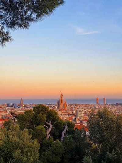 i tetti della città al tramonto visti dall'alto, con le torri della Sagrada Família controluce e il mare all'orizzonte