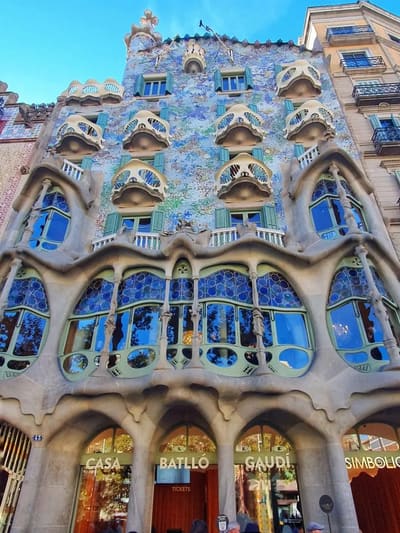 la facciata di Casa Batlló vista dal marciapiede, fra i balconi a maschera e il mosaico azzurro