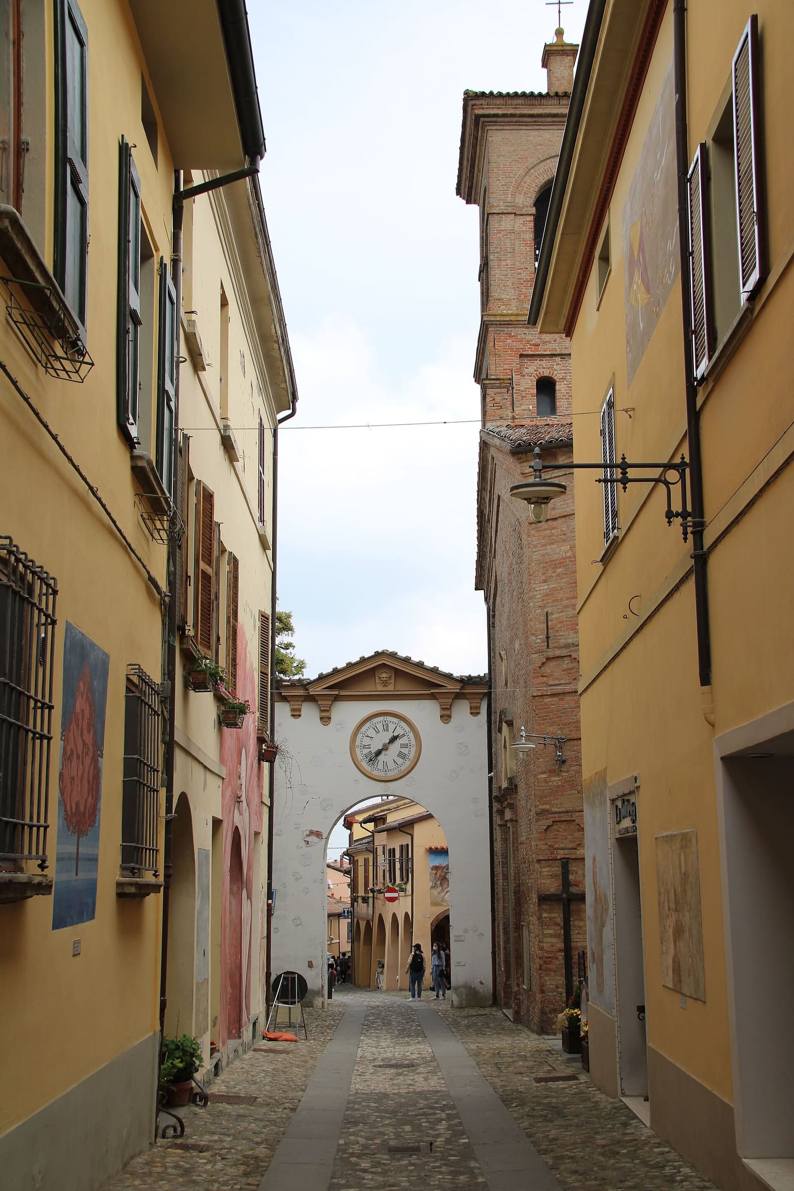 una via del borgo di Dozza, con i muri dipinti e in fondo la porta con l'orologio