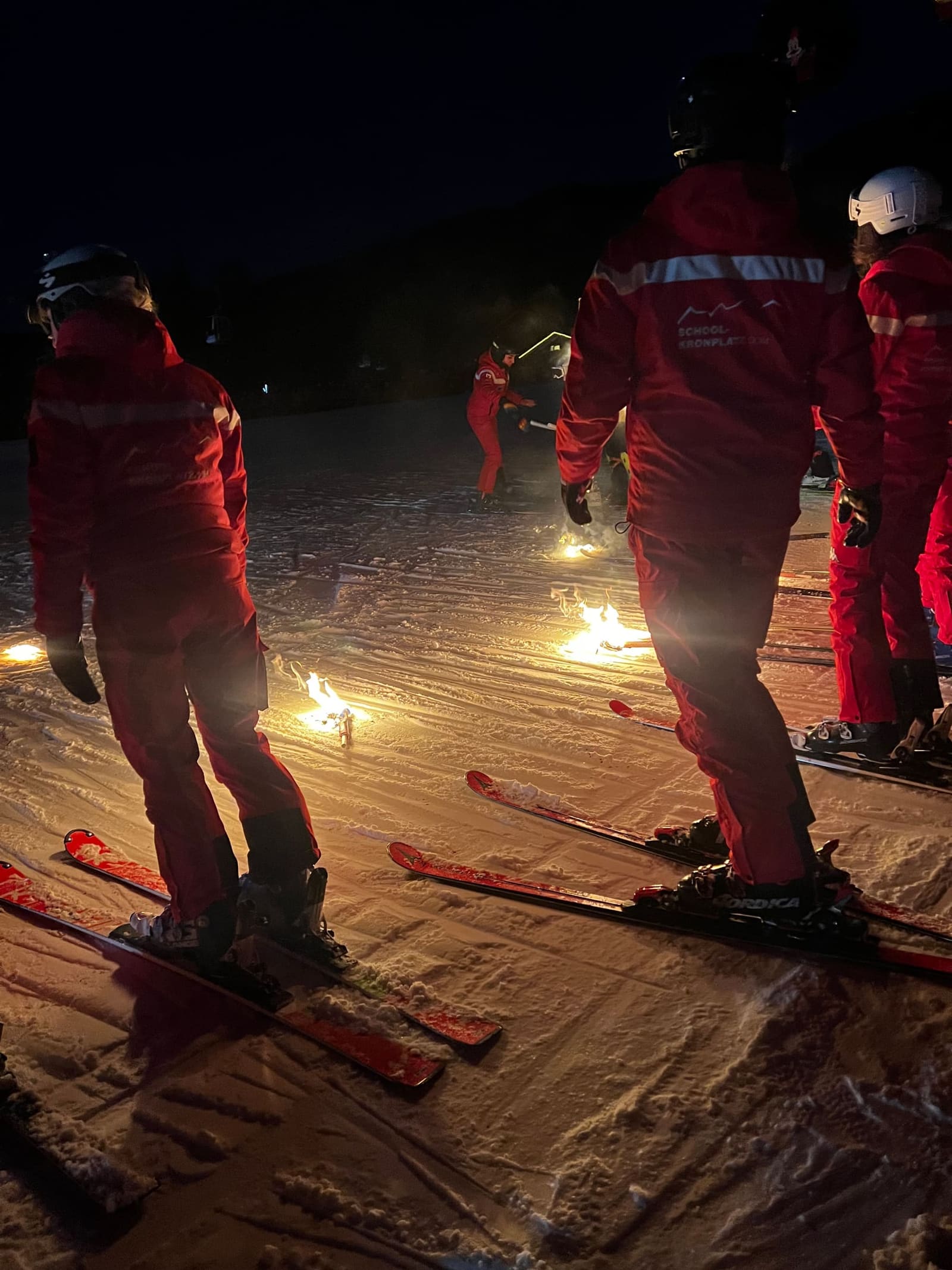 i maestri in fila sulla neve e le fiaccole appoggiate a terra, in attesa