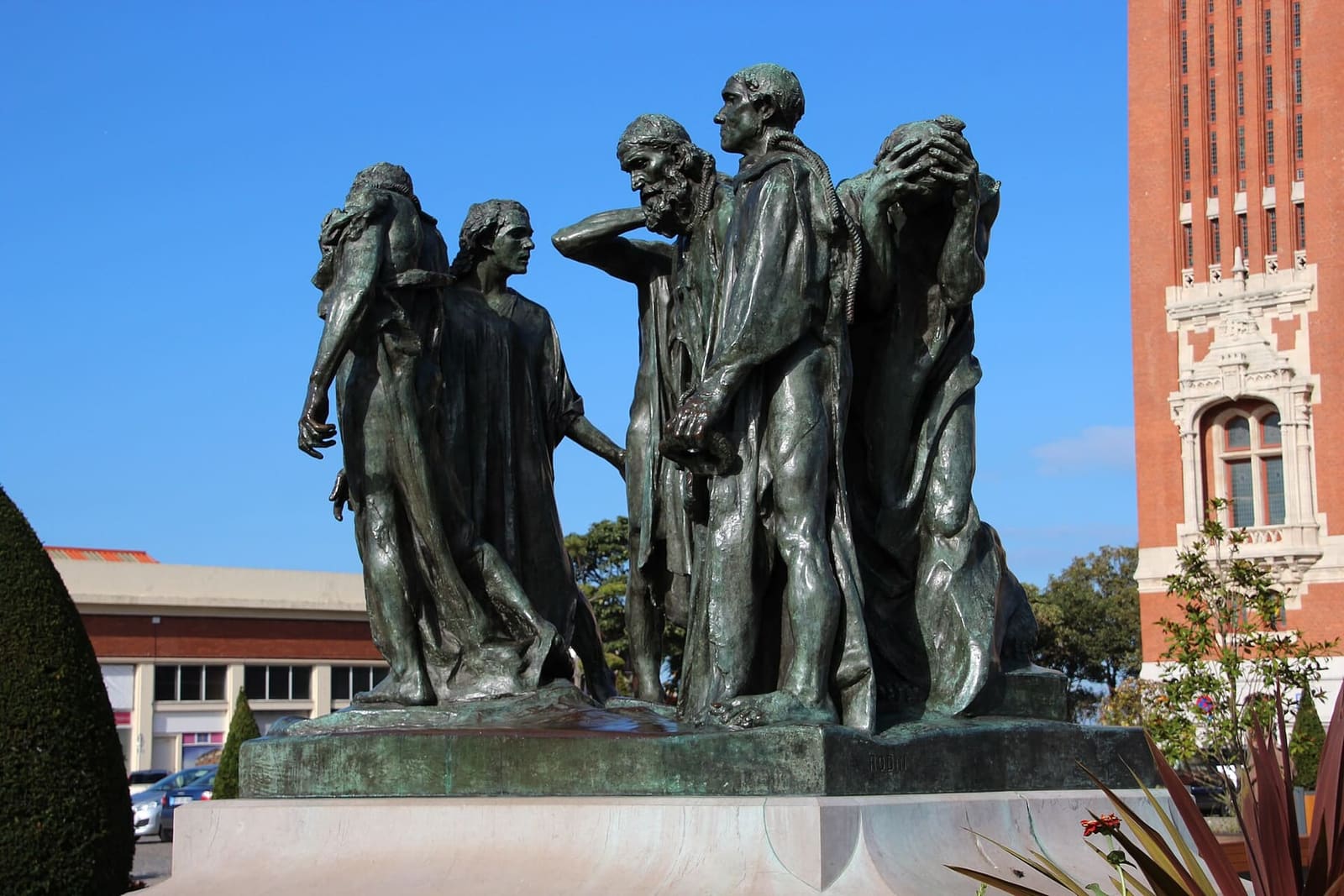 i Bourgeois de Calais di Rodin contro il cielo blu, con un pezzo del beffroi a destra