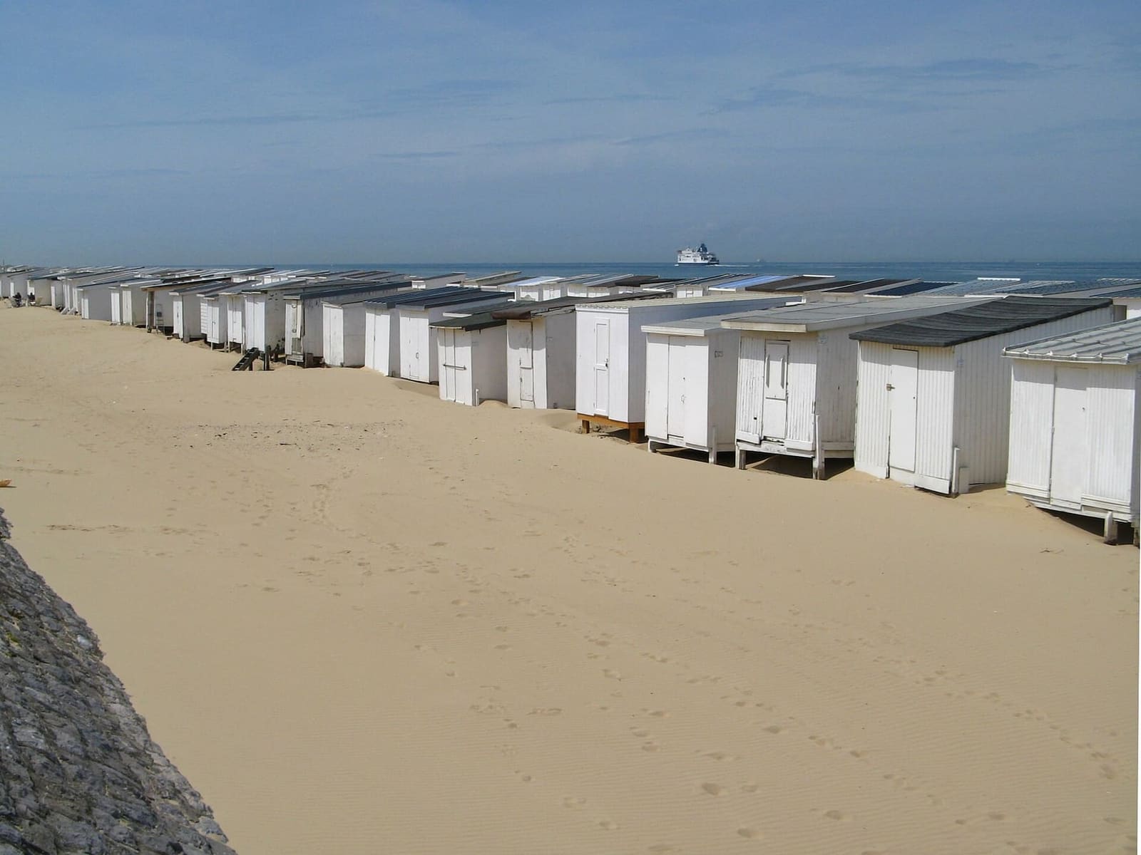 le cabine bianche in fila sulla spiaggia di Calais, con un traghetto all'orizzonte