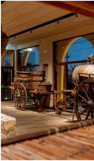 carri, tini e una botte nella sala del museo, con le finestre ad arco sul buio di fuori