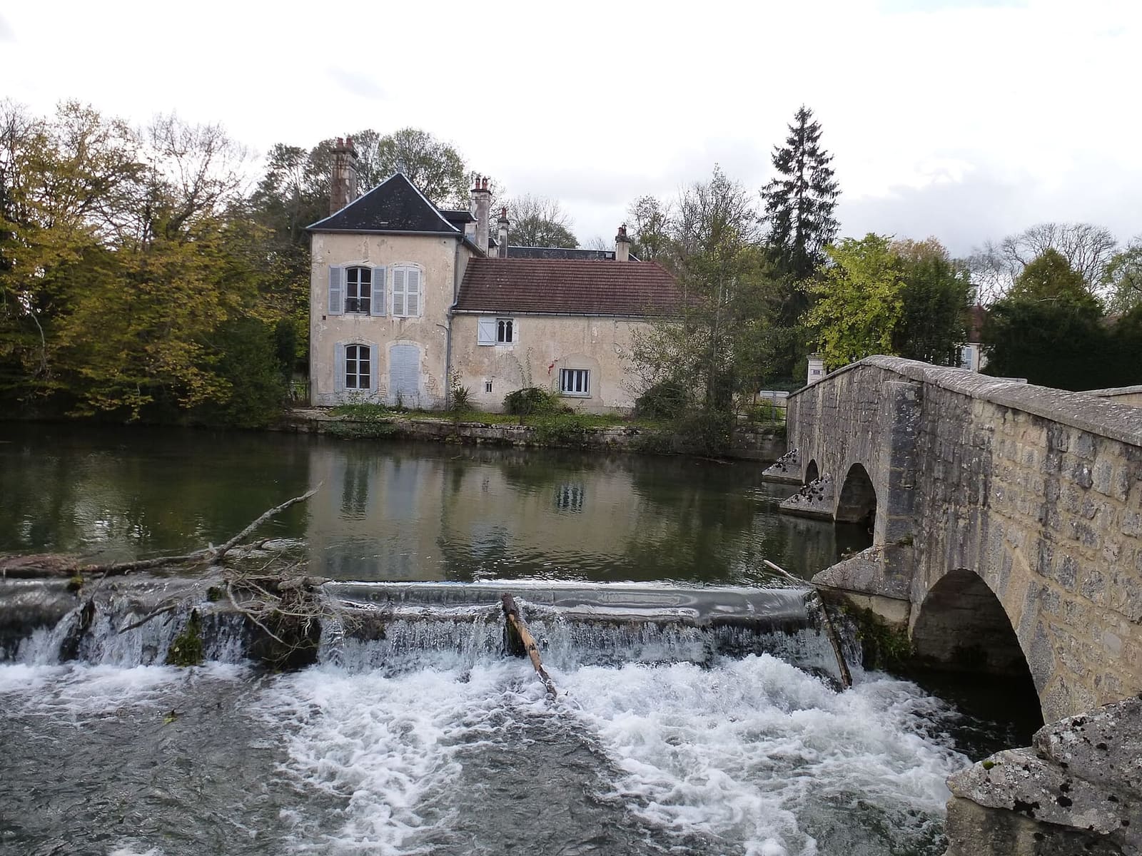 il ponte di pietra sulla Laignes a Les Riceys, con la piccola cascata e una casa sulla riva