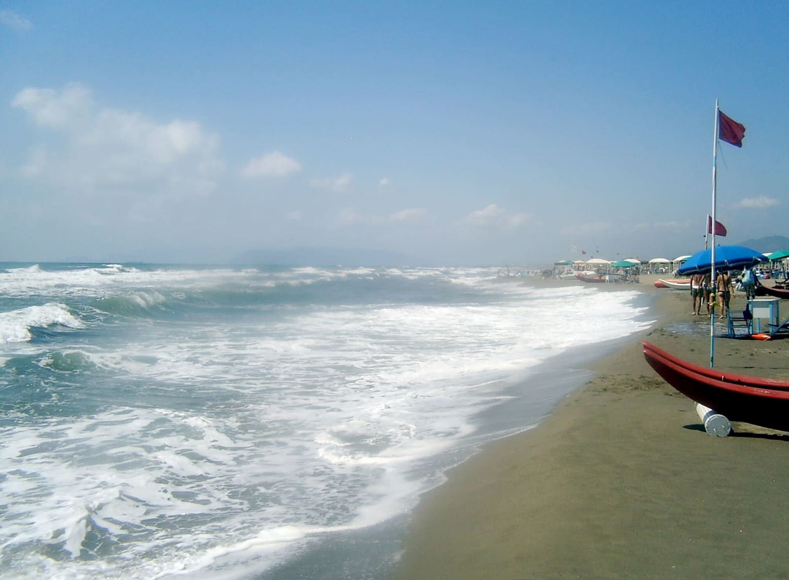 das bewegte Meer am Strand von Forte dei Marmi, mit einem roten Pattino und den Sonnenschirmen