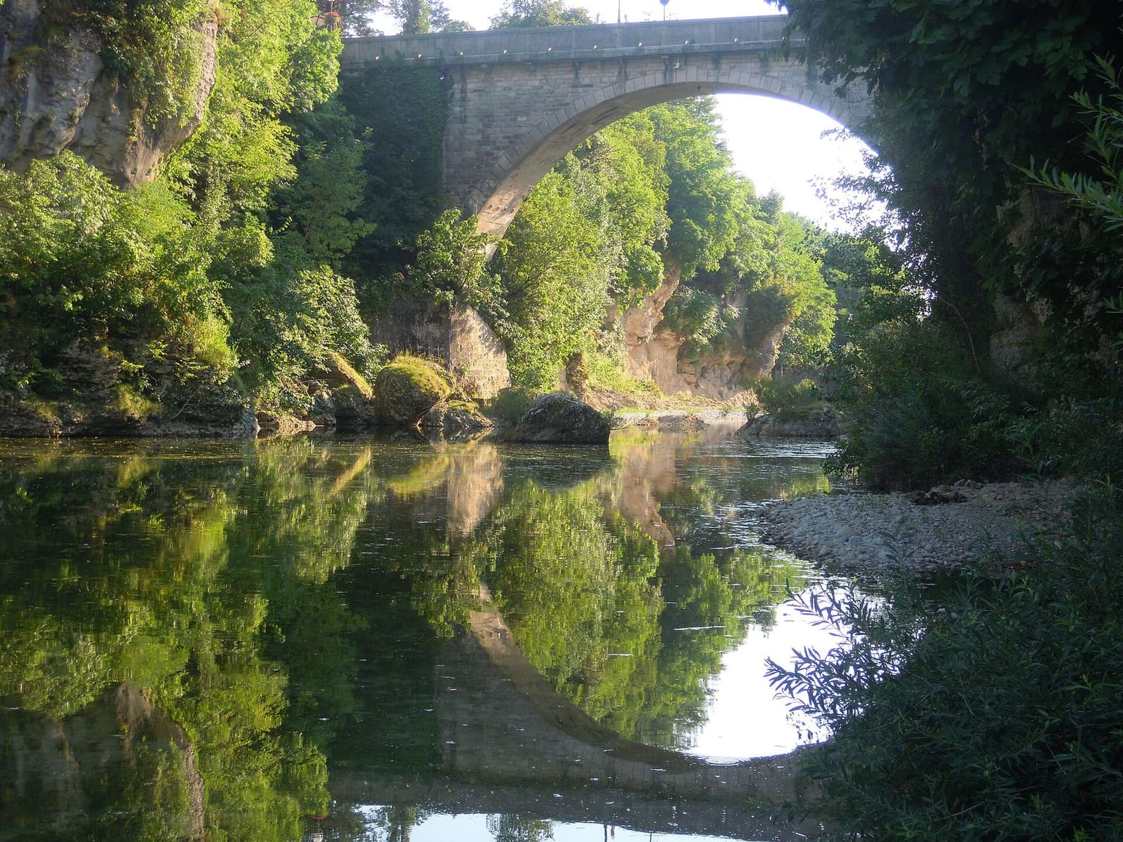 un'arcata del Ponte del Diavolo specchiata nell'acqua del Natisone, fra le rocce della forra
