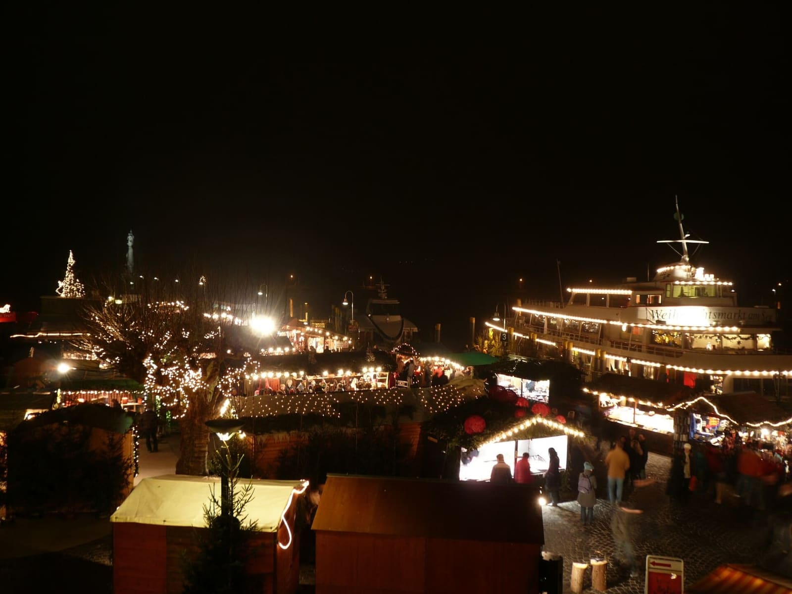 il mercatino di Natale del porto di notte, con una nave illuminata ormeggiata accanto alle casette