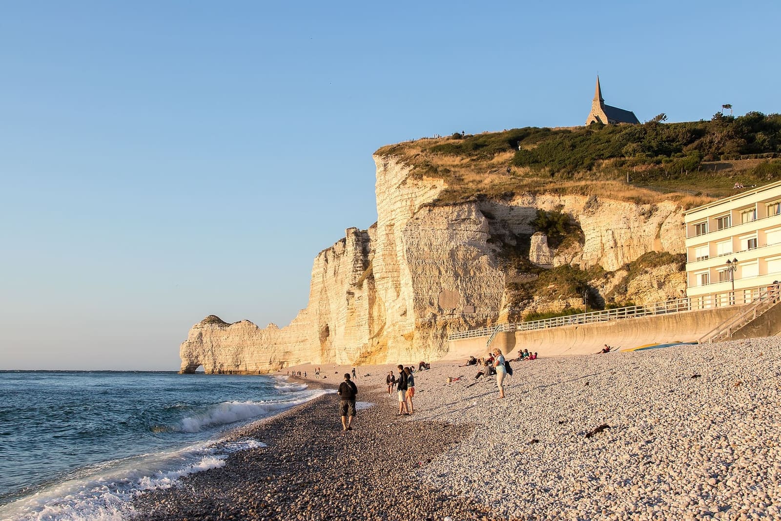 la falaise d'Amont nella luce della sera, con la cappella sul ciglio e la gente sulla spiaggia, ad agosto