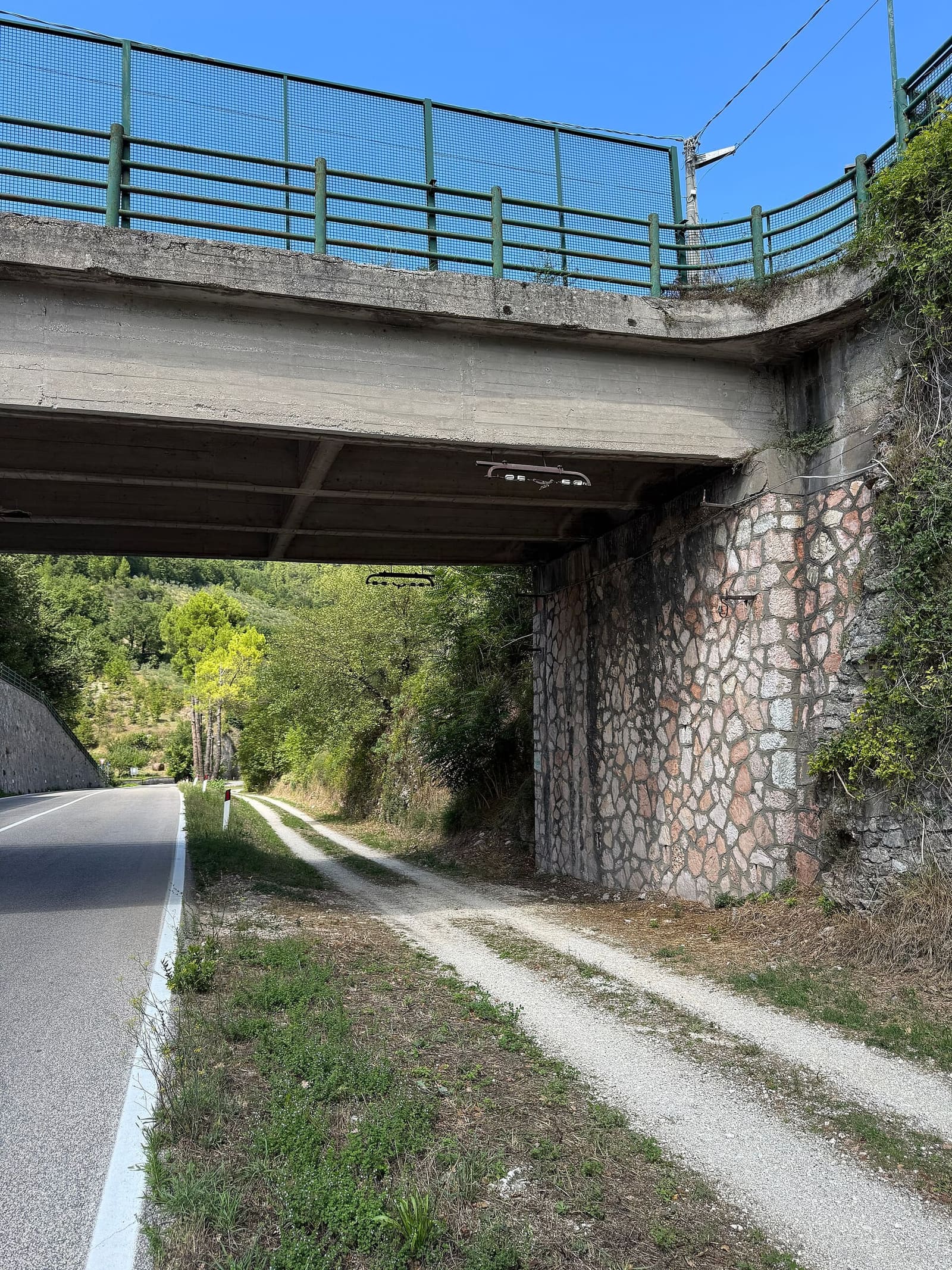 la ciclabile sterrata sulla vecchia ferrovia passa sotto un cavalcavia, accanto alla strada