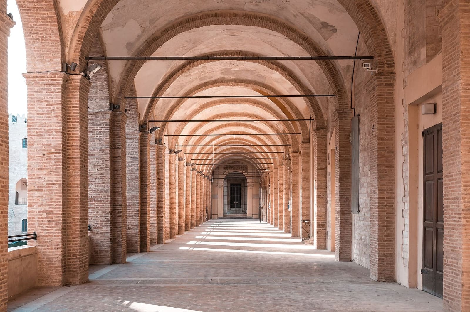 sotto il loggiato, con le volte in fila che si rimpiccioliscono fino in fondo e la luce che entra dagli archi