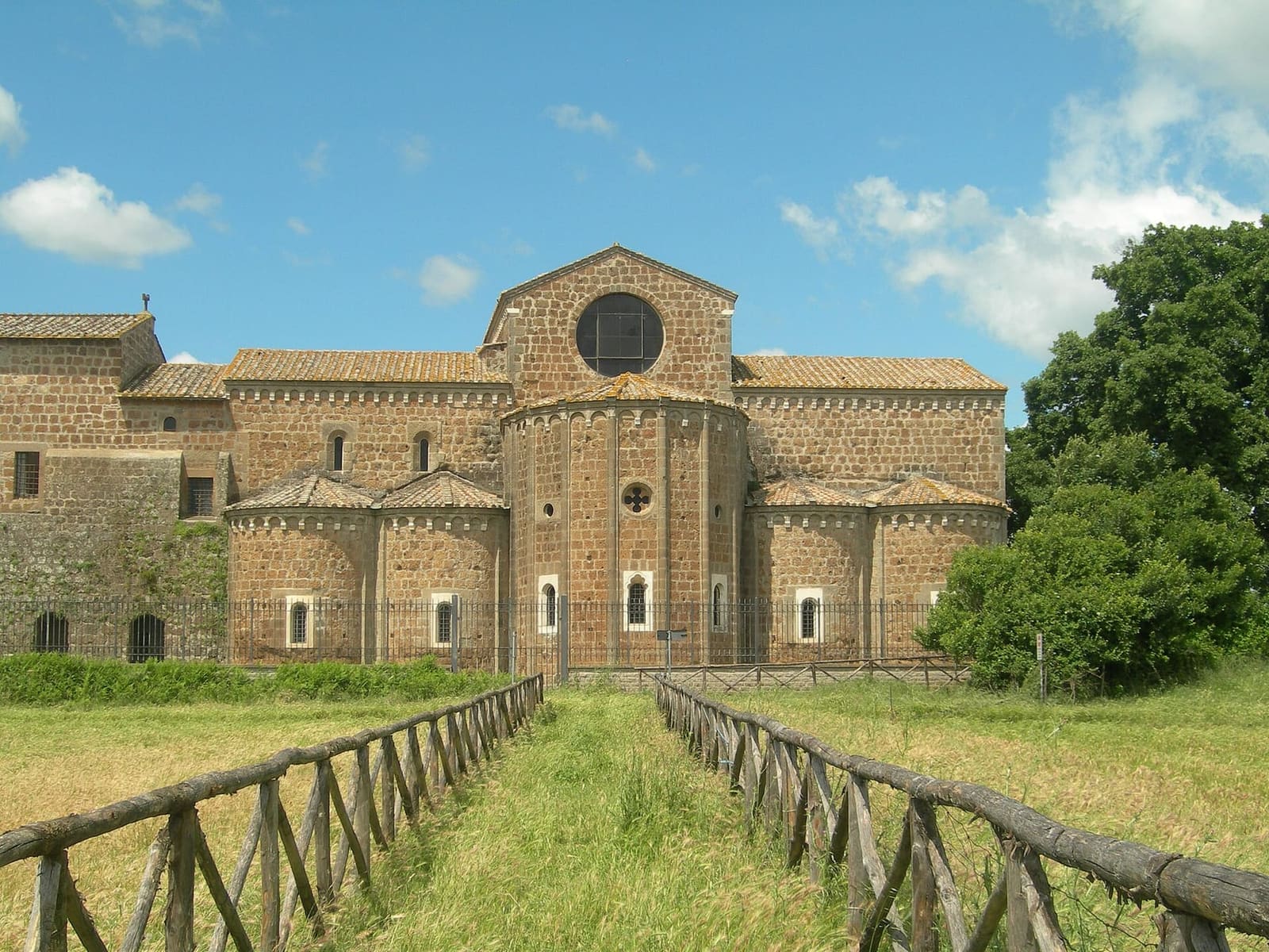 l'abbazia di Santa Maria di Falleri dal sentiero fra gli steccati: il lato delle absidi, il rosone in alto e il tufo bruno del XII secolo