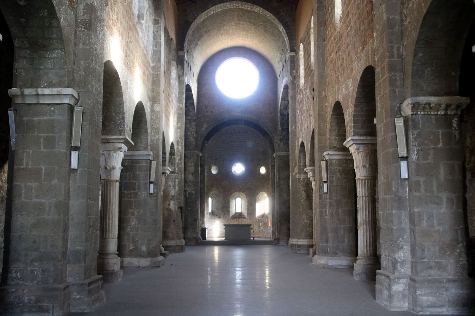 dentro l'abbazia: la navata centrale fra i pilastri e le colonne, il pavimento lucido e in fondo l'abside con il rosone