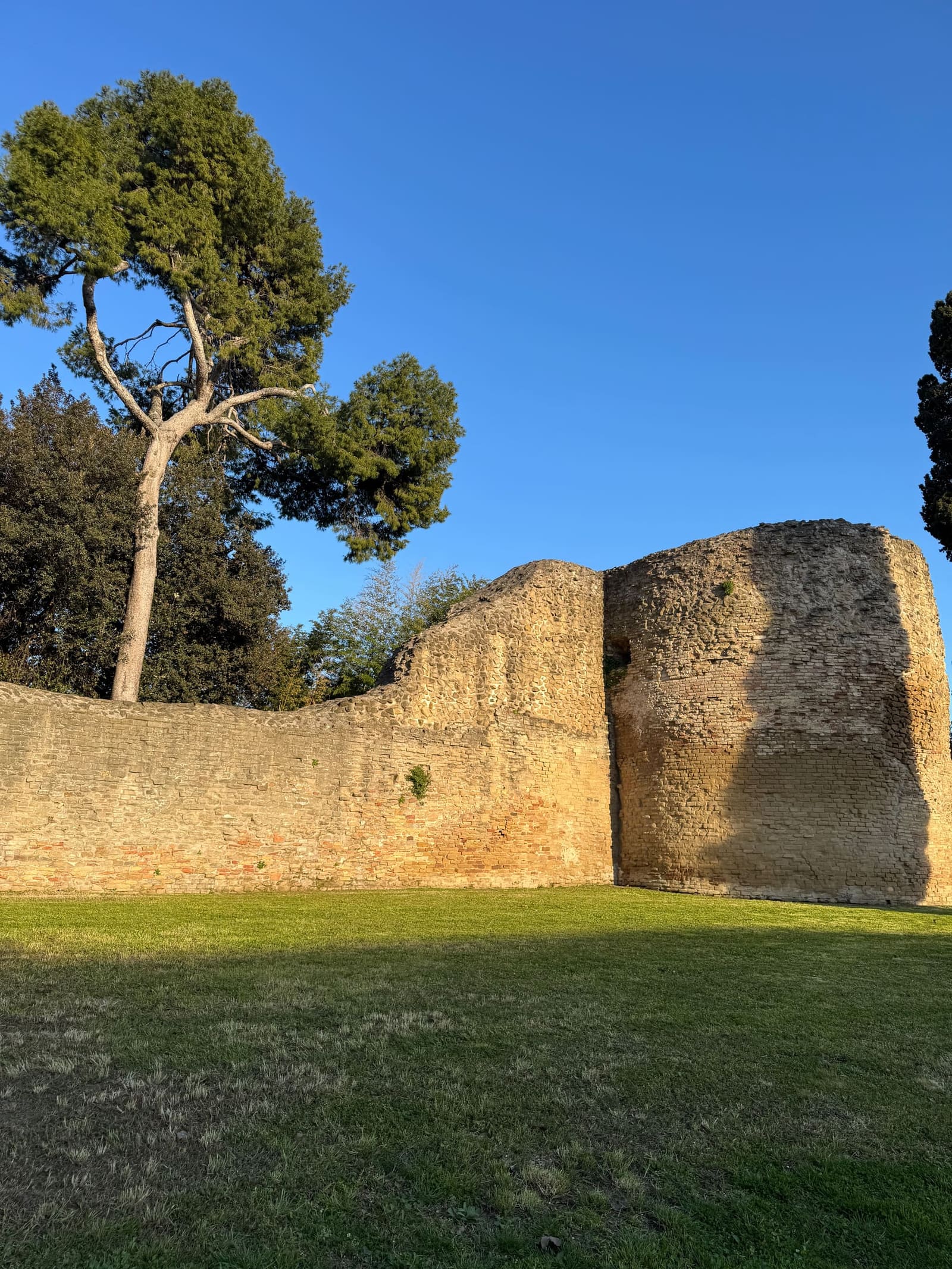il torrione rotondo delle mura augustee nel prato, con la luce di fine pomeriggio