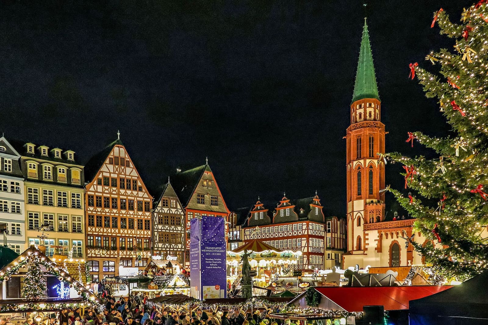 la Ostzeile e l'Alte Nikolaikirche di notte, sopra le casette del mercatino e l'albero illuminato