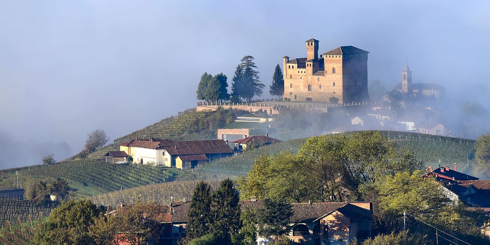 il castello sopra la nebbia, con gli alberi e il campanile della chiesa accanto