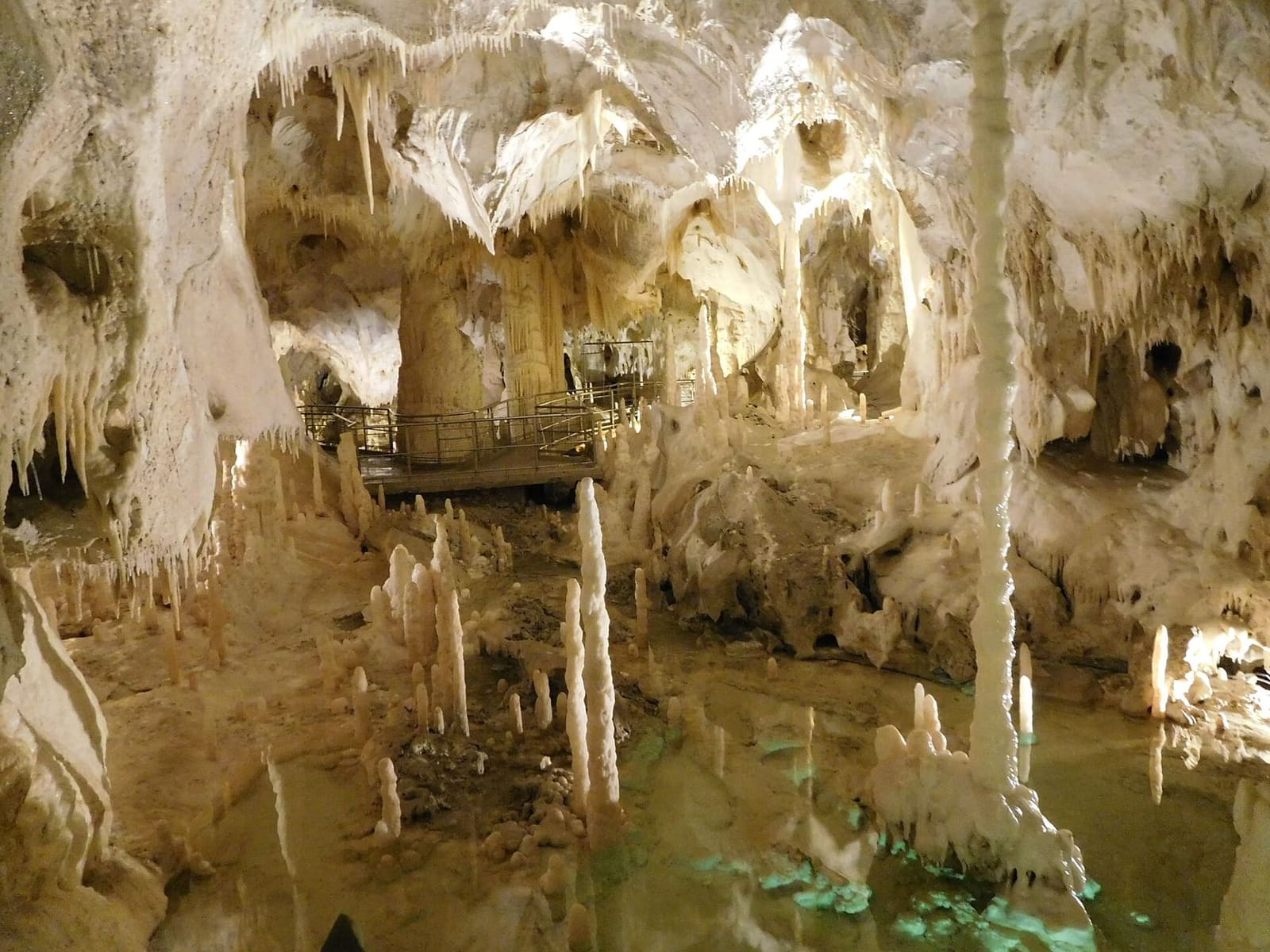 il lago verde chiaro fra le stalagmiti, con la passerella che lo scavalca in fondo