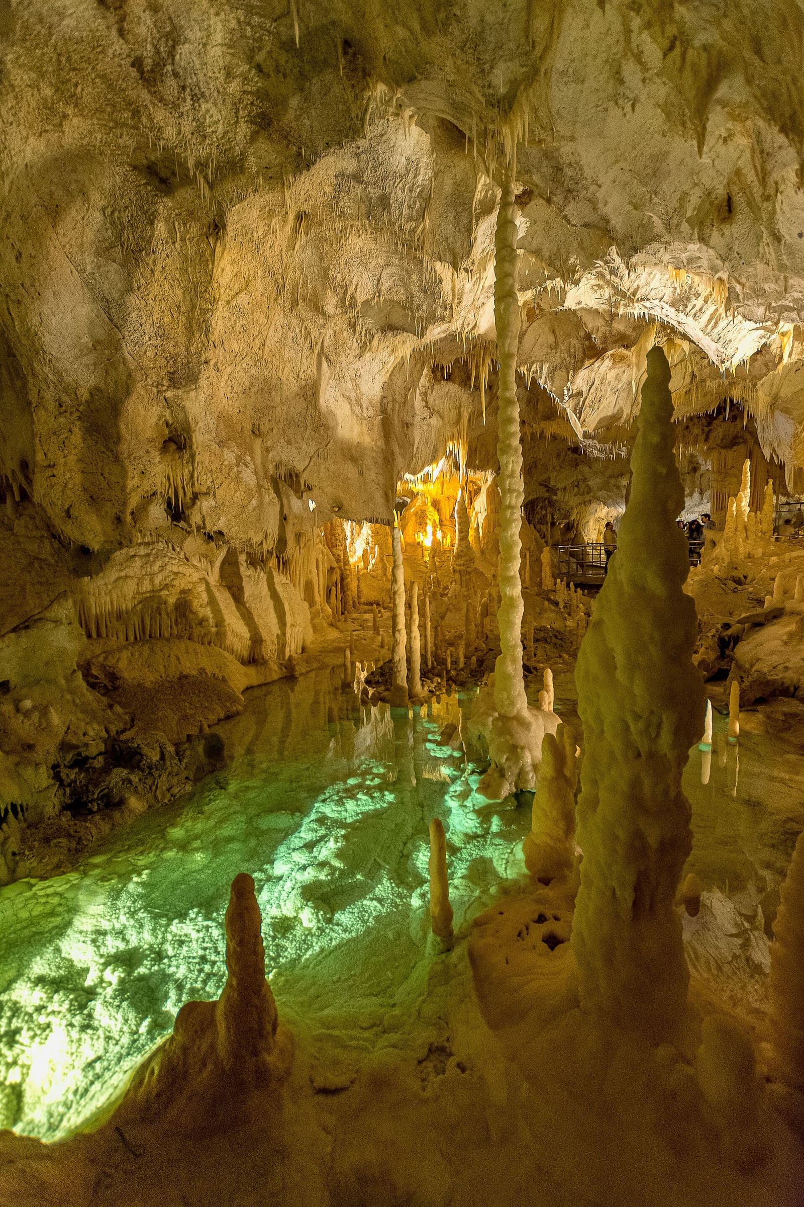 l'acqua illuminata di verde ai piedi delle stalagmiti, e sul fondo la luce gialla della sala dopo