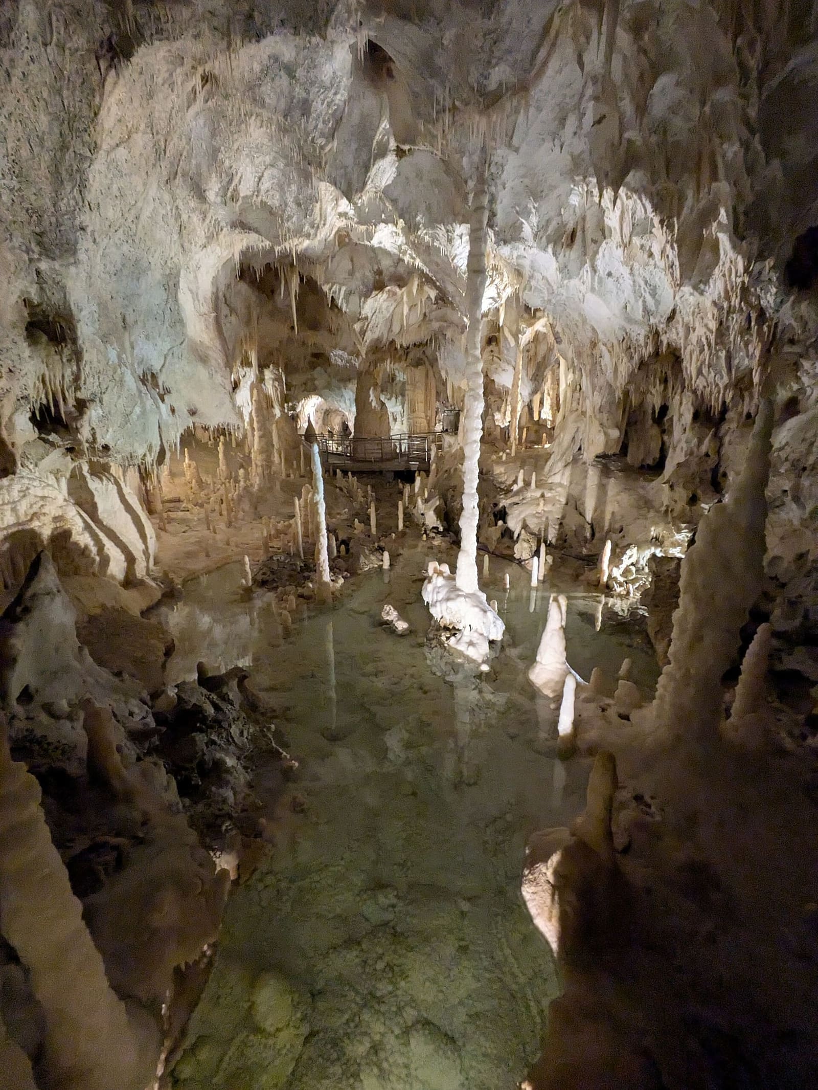 una pozza d'acqua limpida con una stalagmite bianca nel mezzo e le colonne sottili intorno