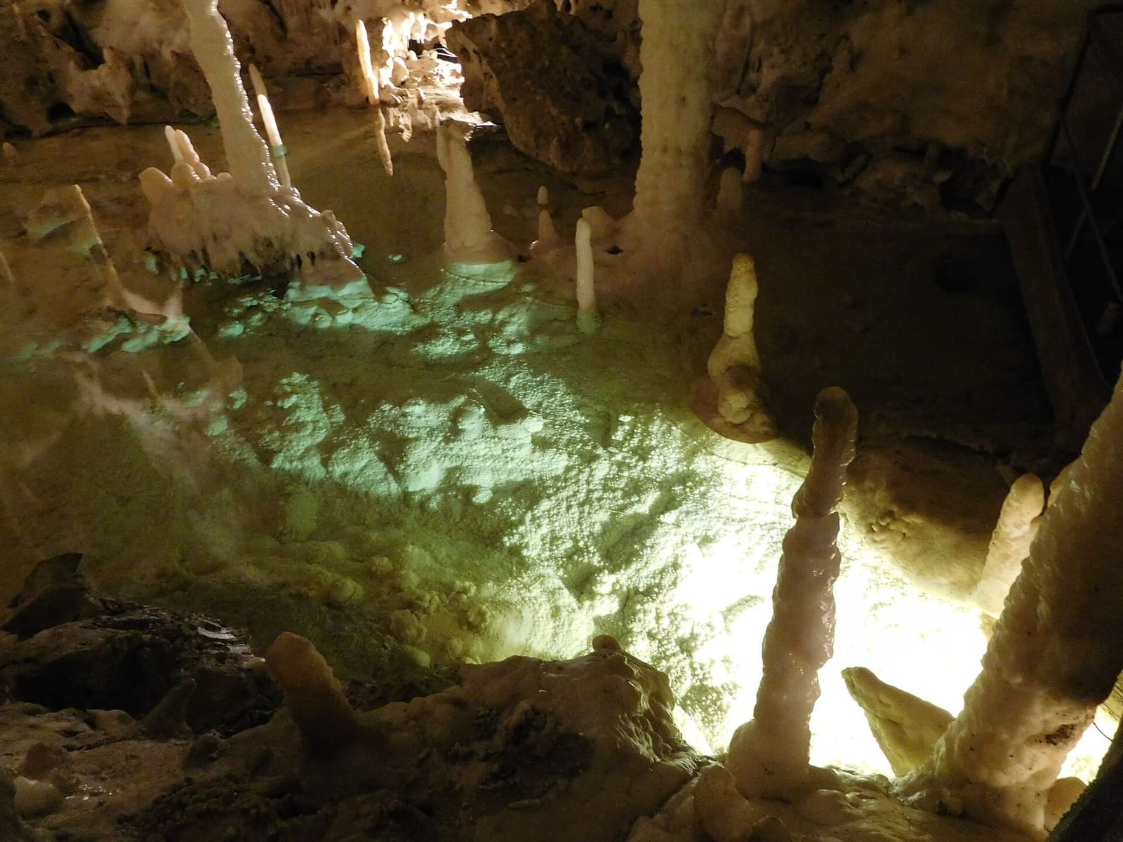 una pozza illuminata di verde sotto le concrezioni, con l'acqua così ferma che non si vede