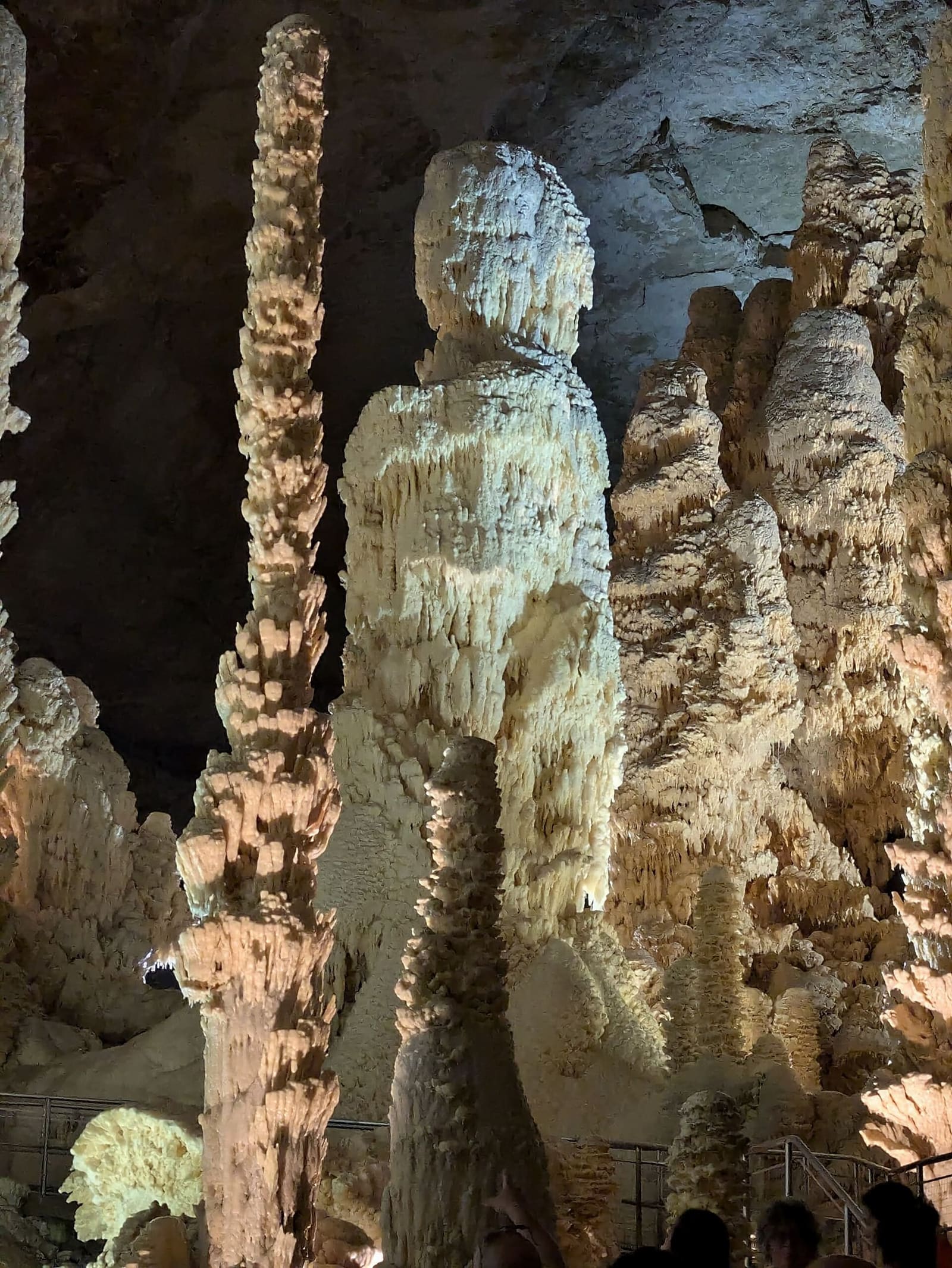 una stalagmite larga e arrotondata che sembra una statua, con accanto una colonna sottile e nodosa