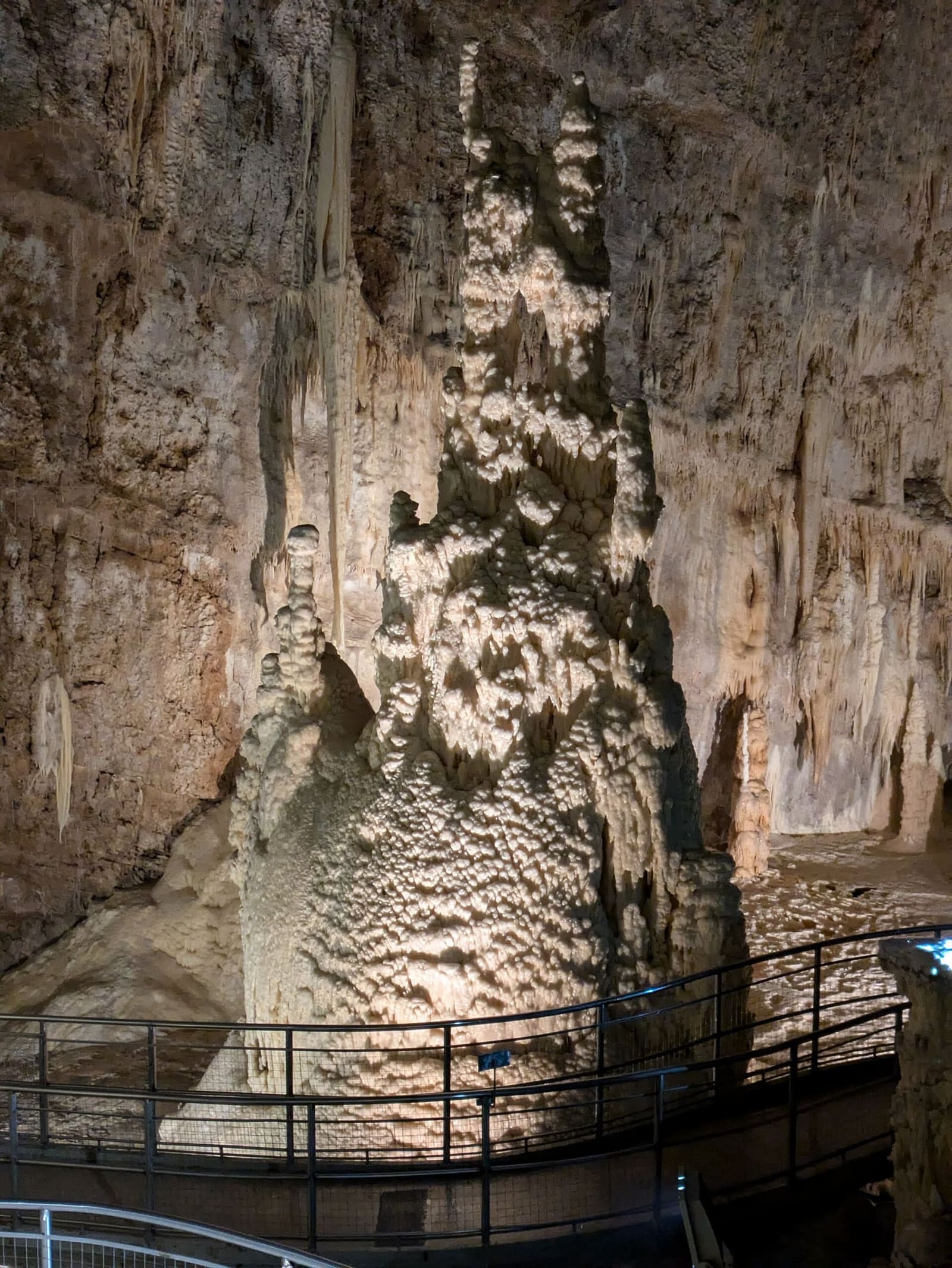 una stalagmite enorme che sale accanto alla passerella: il corrimano alla sua base dà la misura
