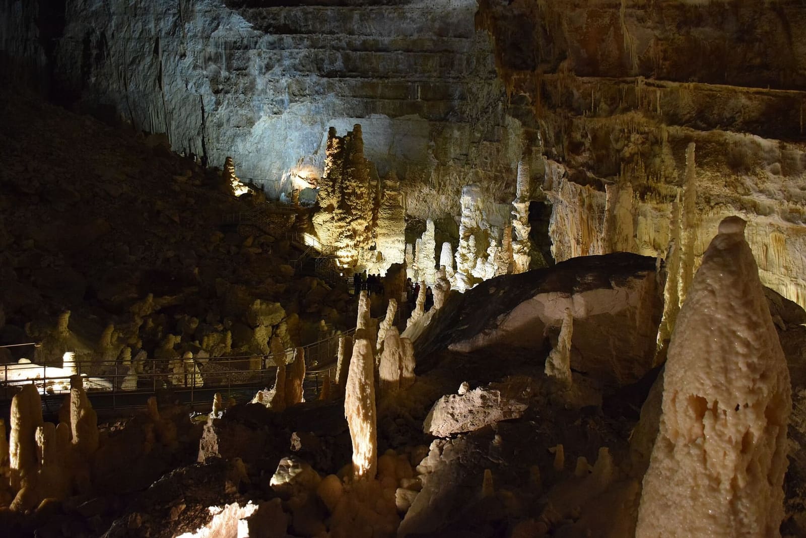 le stalagmiti illuminate una per una nel buio della sala, e a sinistra il corrimano della passerella