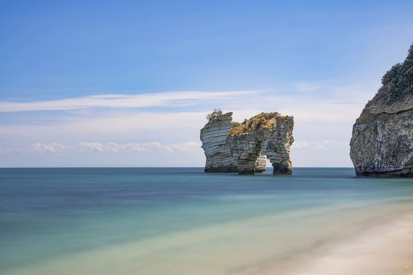 un faraglione visto dalla spiaggia delle Zagare, con l'acqua bassa e chiara