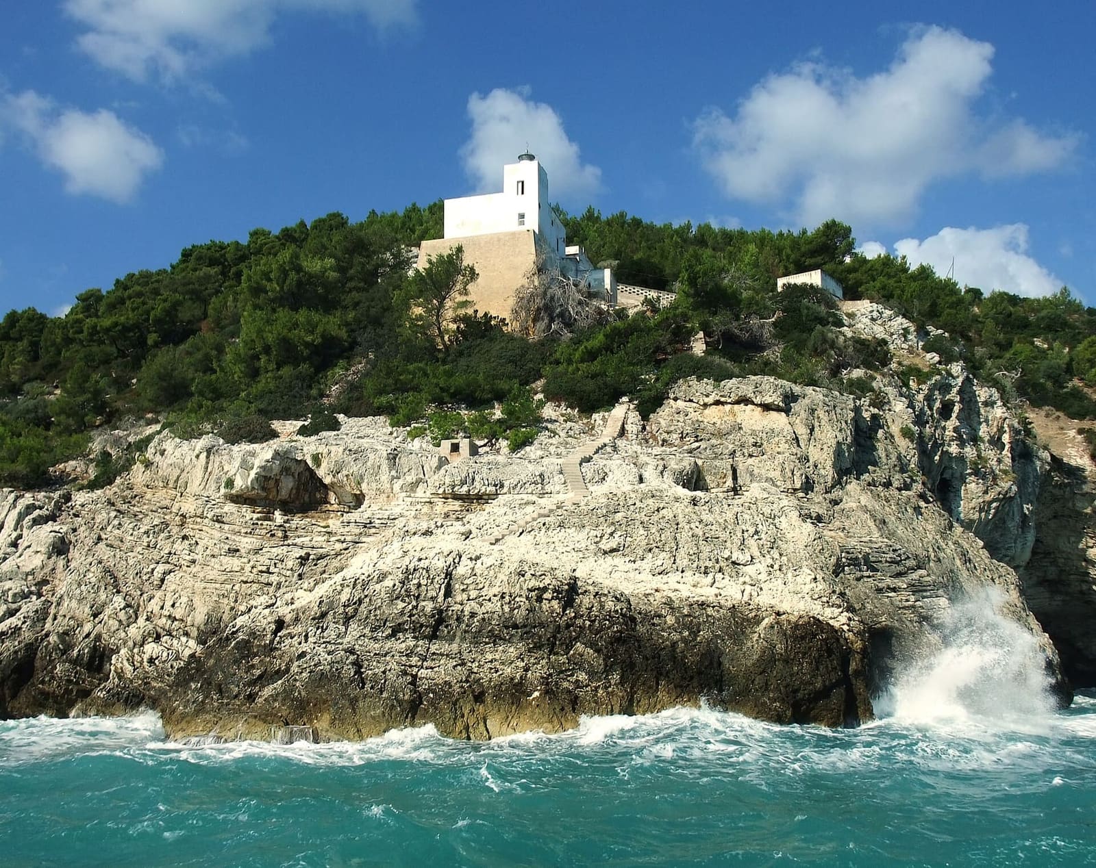 una casa bianca in cima a un promontorio, con le onde che si rompono sotto