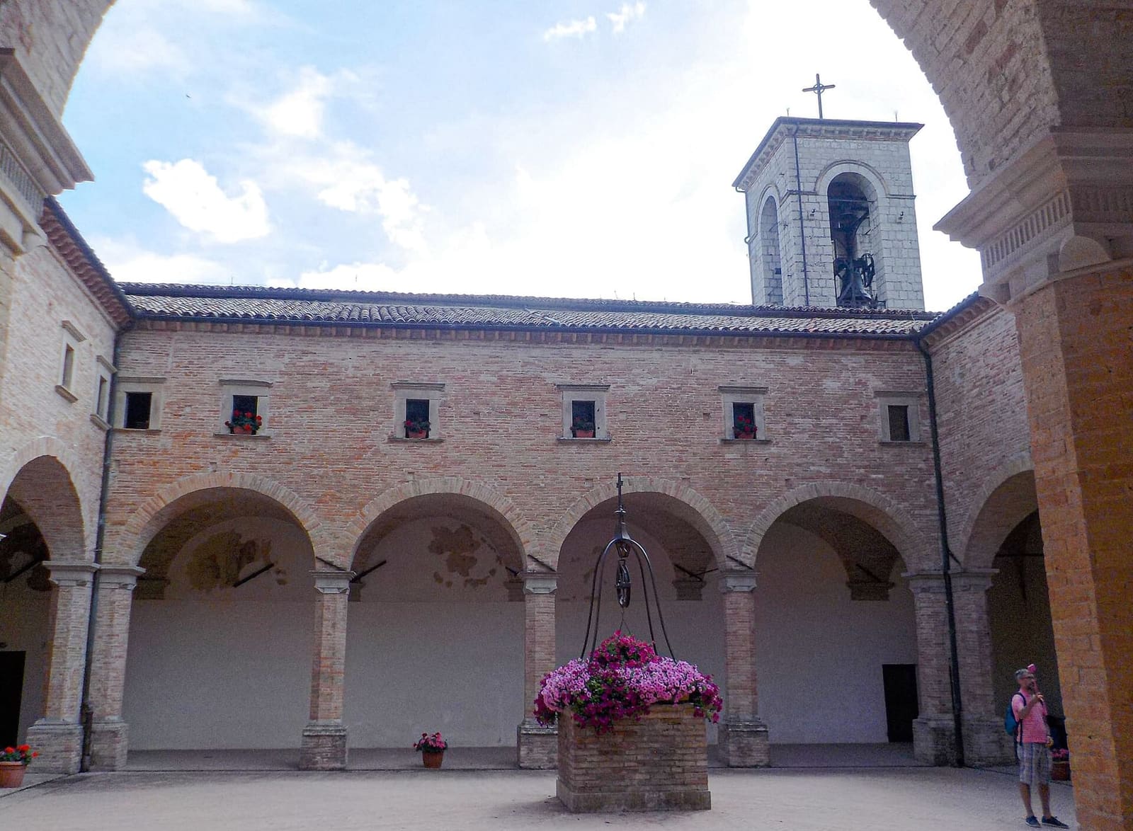 il chiostro di mattoni della basilica, con il pozzo fiorito in mezzo e il campanile sopra le arcate