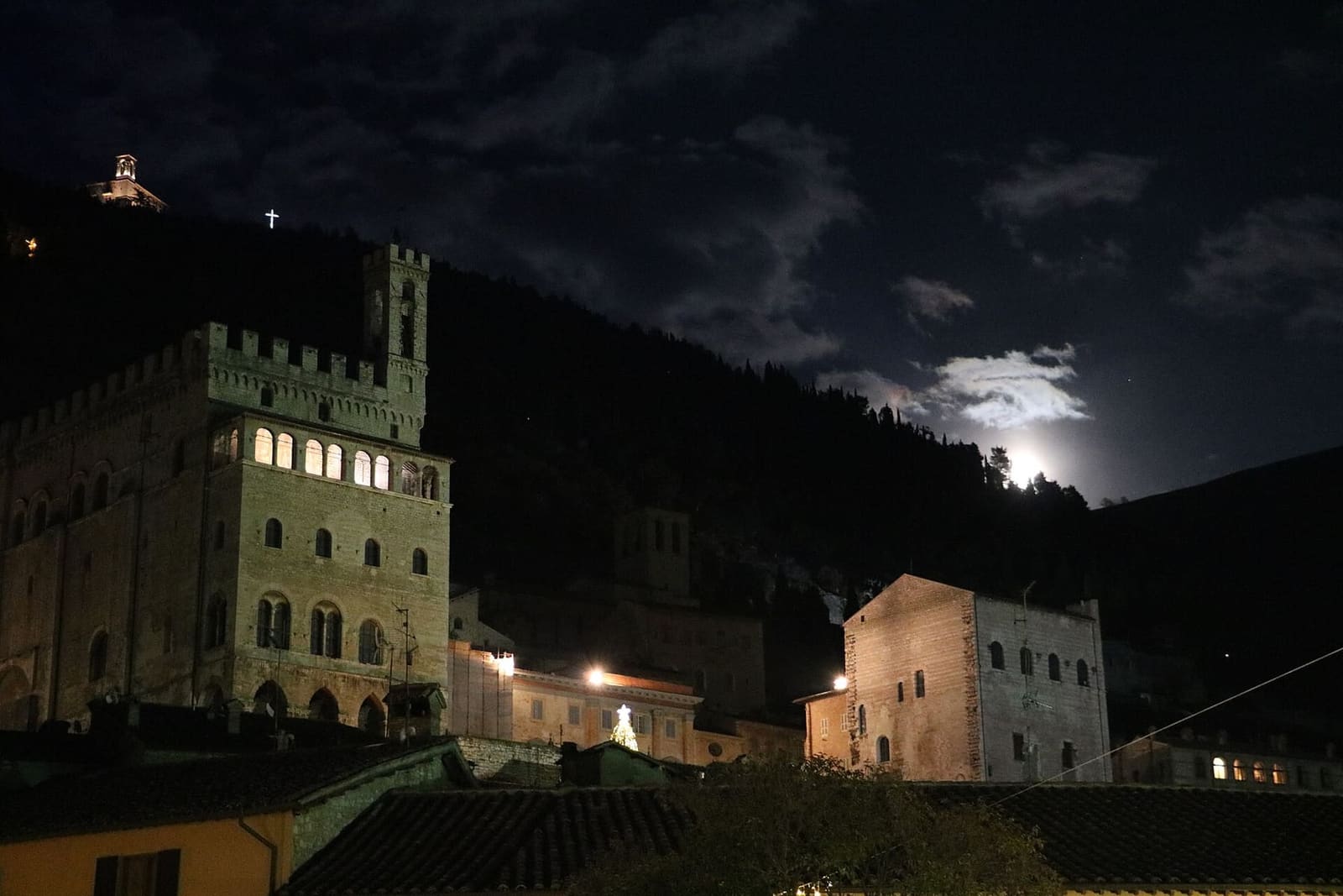 il Palazzo dei Consoli e il Palazzo Pretorio di notte, con la luna che sorge dietro il monte e la basilica accesa in cima