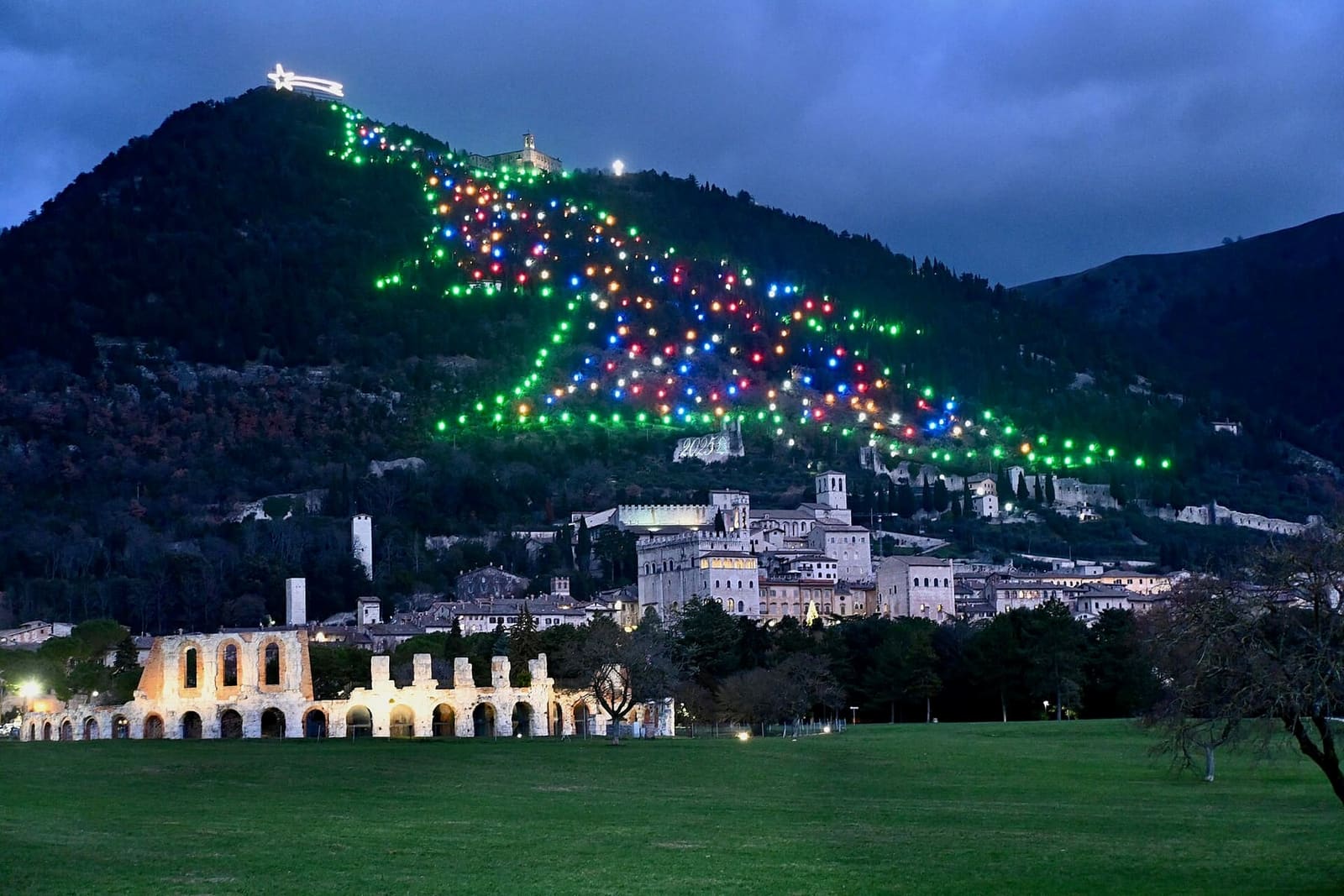 l'albero di Natale disegnato con le luci sul fianco del monte Ingino, sopra la città e le arcate del teatro romano illuminate