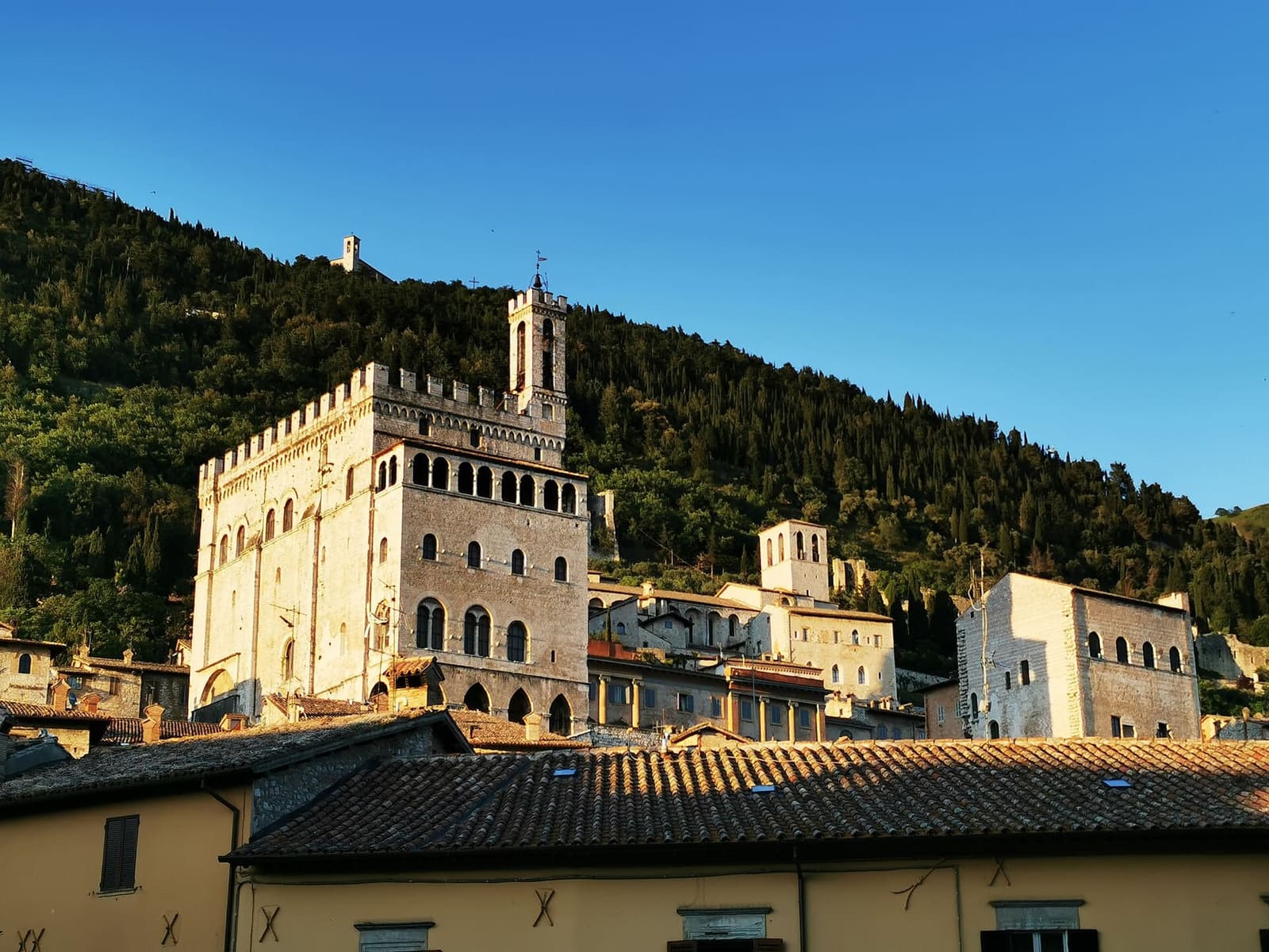 il Palazzo dei Consoli nella luce bassa sopra i tetti, con il Palazzo Pretorio a destra, il monte Ingino dietro e la basilica di Sant'Ubaldo in cima