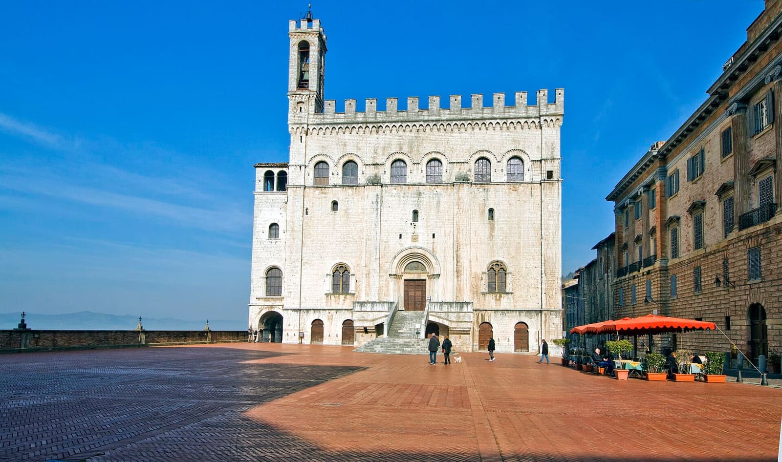 piazza Grande con il Palazzo dei Consoli bianco di sole e il Palazzo Ranghiasci a destra