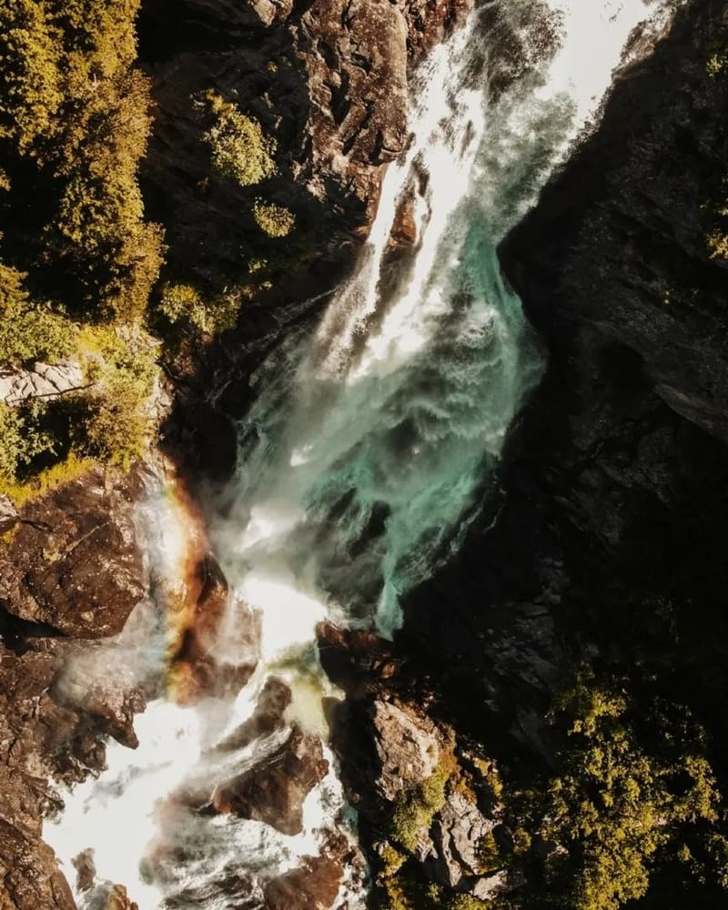 la cascata vista dall'alto fra le rocce, con l'acqua turchese e un arcobaleno nella nebbia