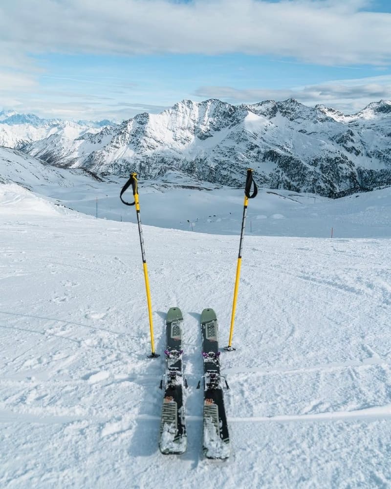 un paio di sci e i bastoncini piantati sulla pista, davanti alle cime innevate