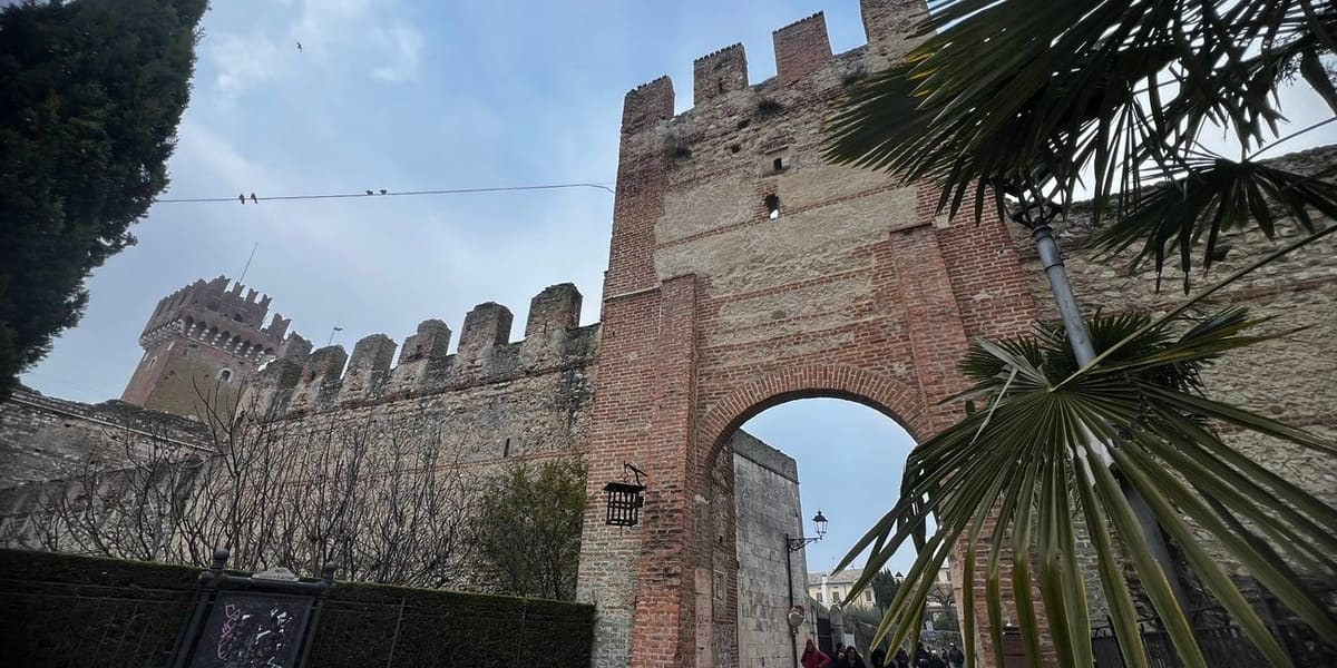 la porta ad arco nelle mura merlate, con il mastio del castello scaligero sullo sfondo