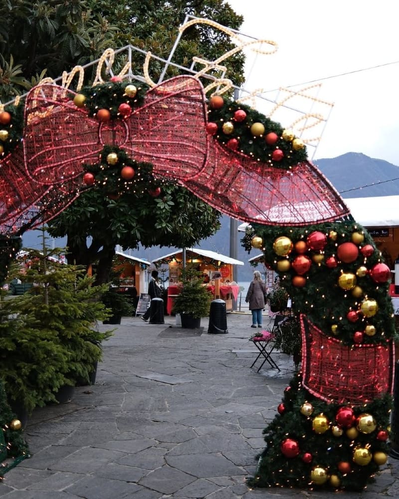 l'arco di rami e fiocchi rossi all'ingresso del mercatino di Natale, con le casette di legno e il lago