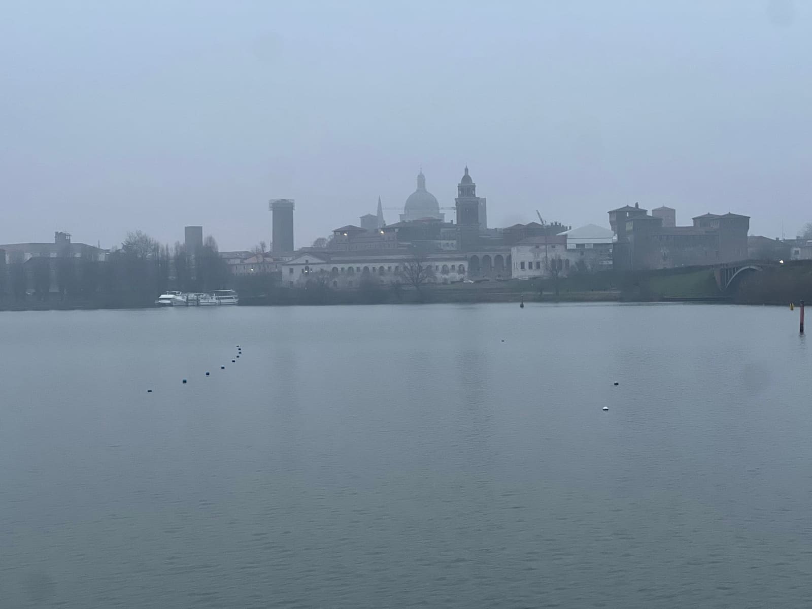 lo skyline di Mantova dall'altra riva del lago di Mezzo nella foschia, la cupola di Sant'Andrea e il Palazzo Ducale