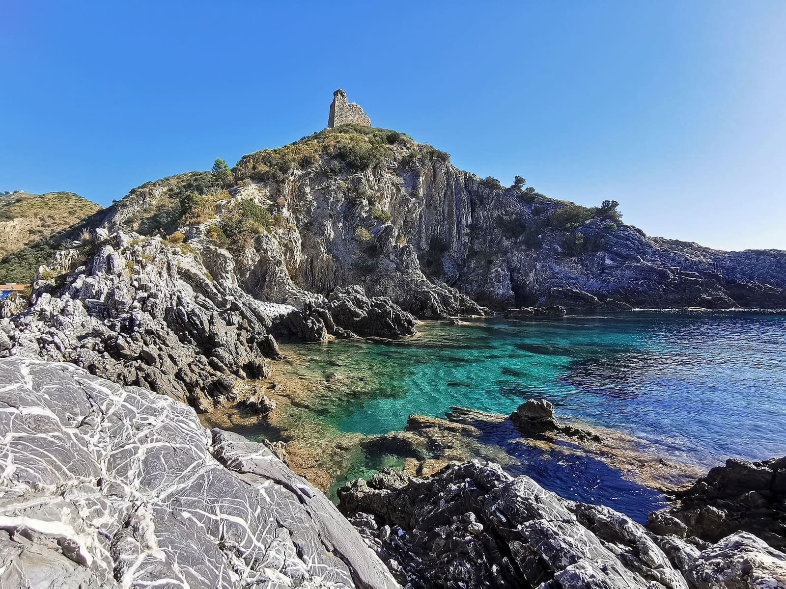 la Punta del Telegrafo con la torre in cima e l'acqua chiara fra gli scogli, a novembre