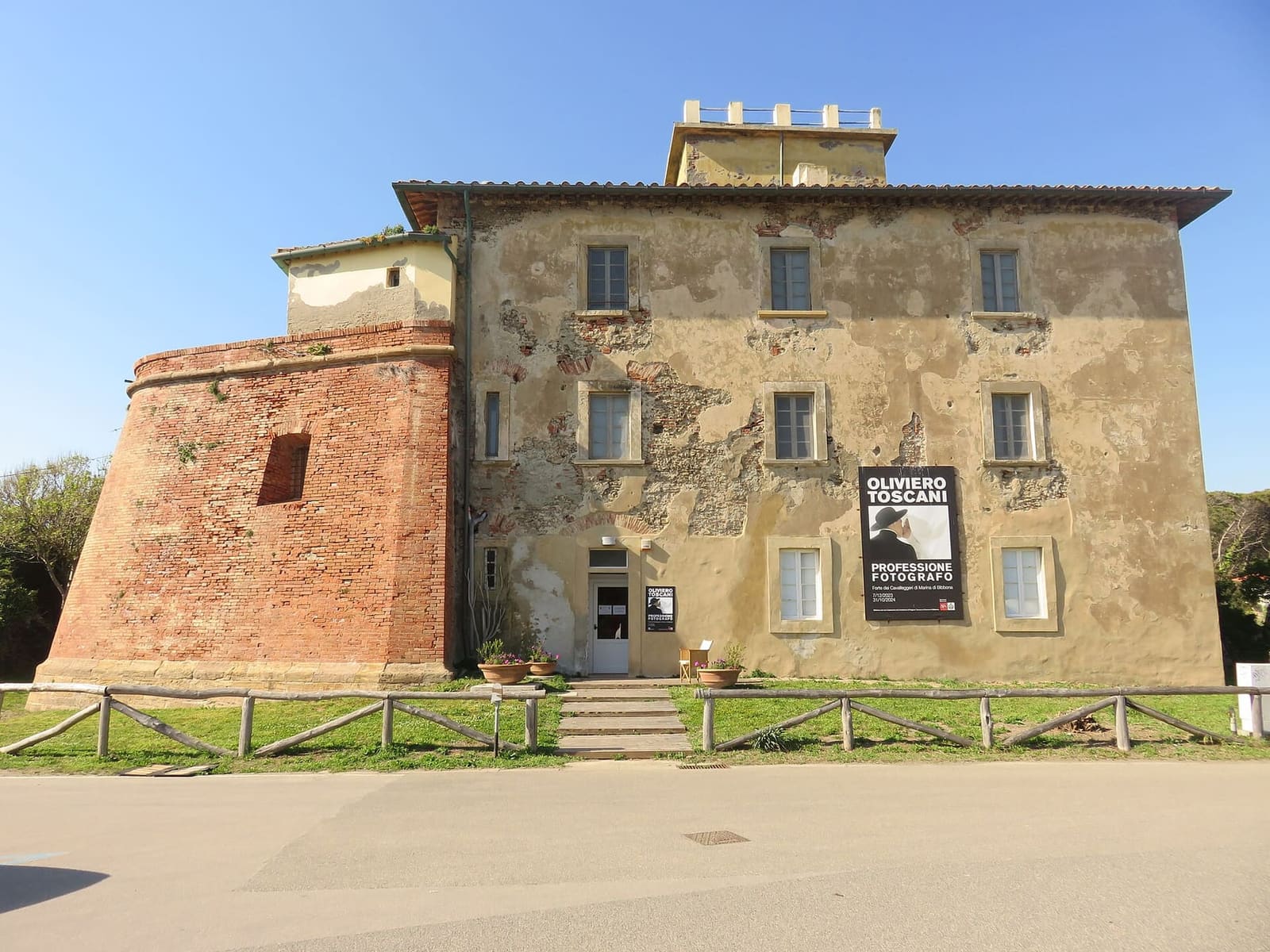la facciata del Forte verso la strada, con il bastione di mattoni, l'intonaco consumato e il manifesto di una mostra all'ingresso