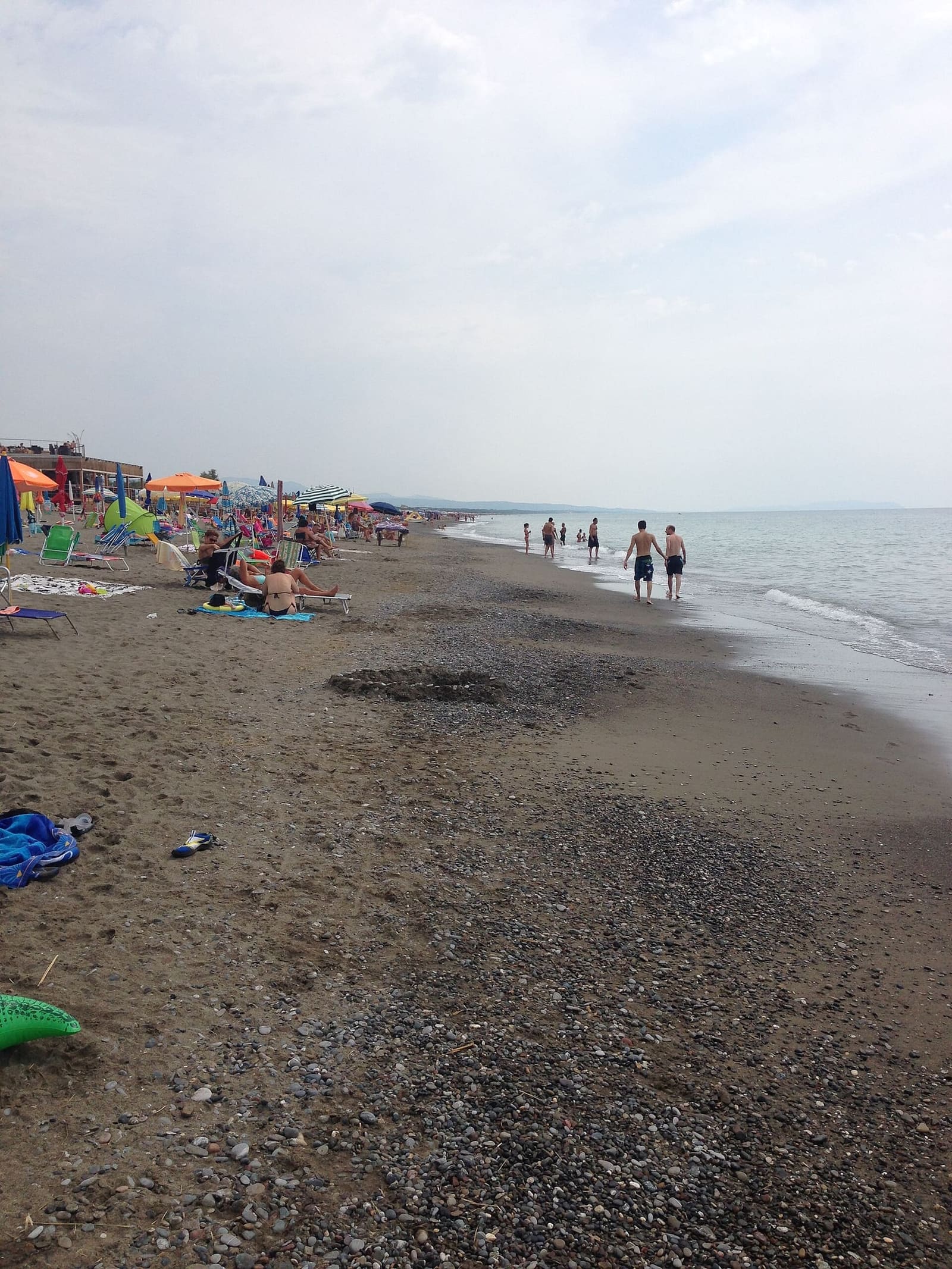 la spiaggia larga di sabbia e ciottoli a metà agosto, con gli ombrelloni da una parte e la riva che si perde in lontananza