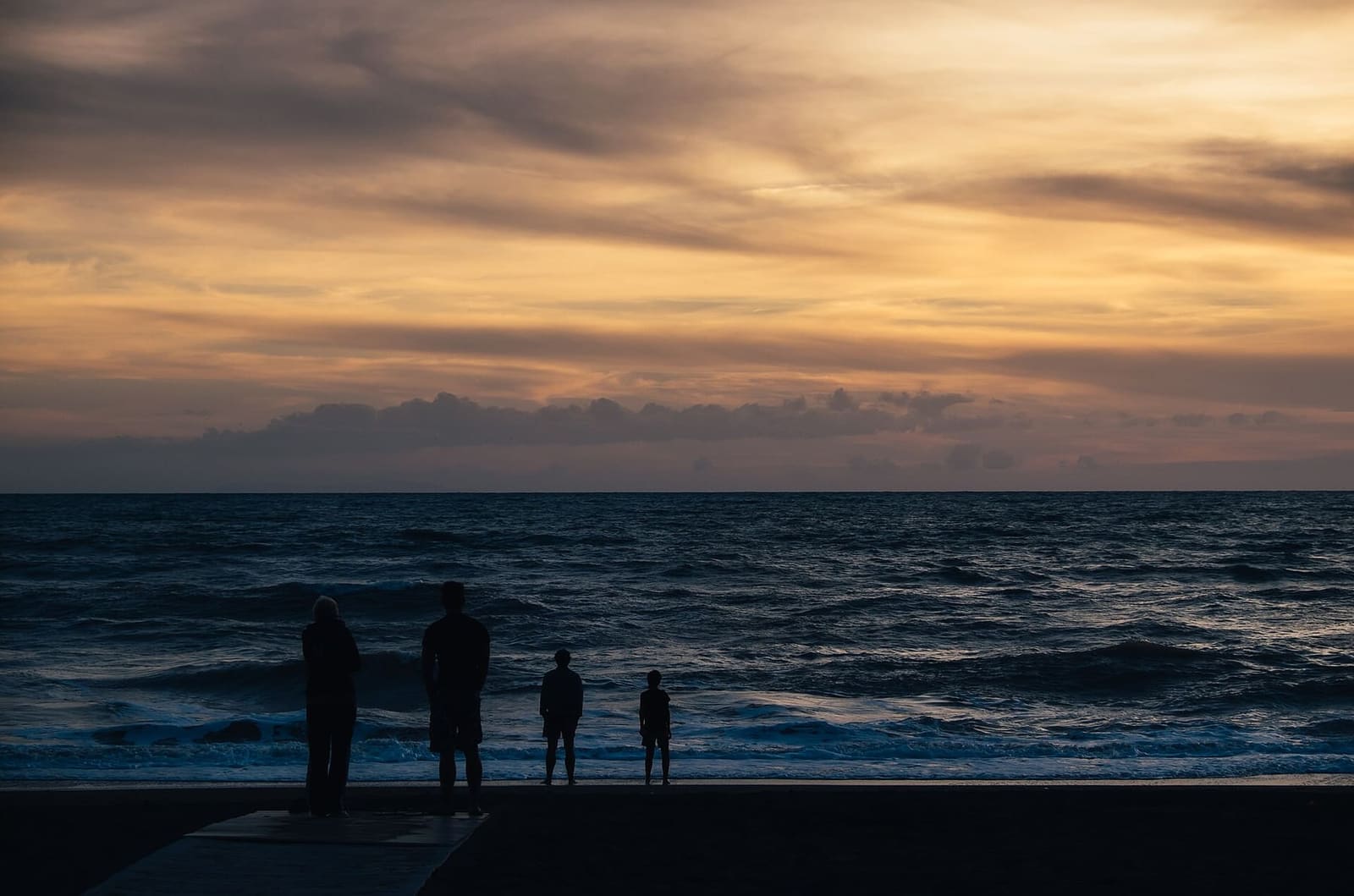 il cielo del crepuscolo sopra il mare, con le sagome scure di quattro persone sulla riva