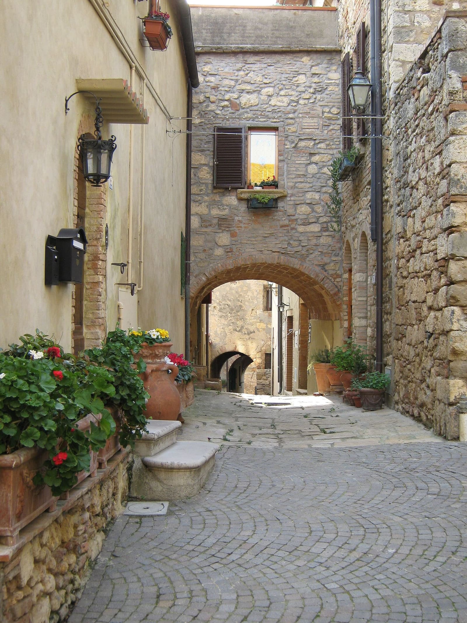 un vicolo lastricato del borgo di Bibbona, con i gerani sui muri e un arco in fondo