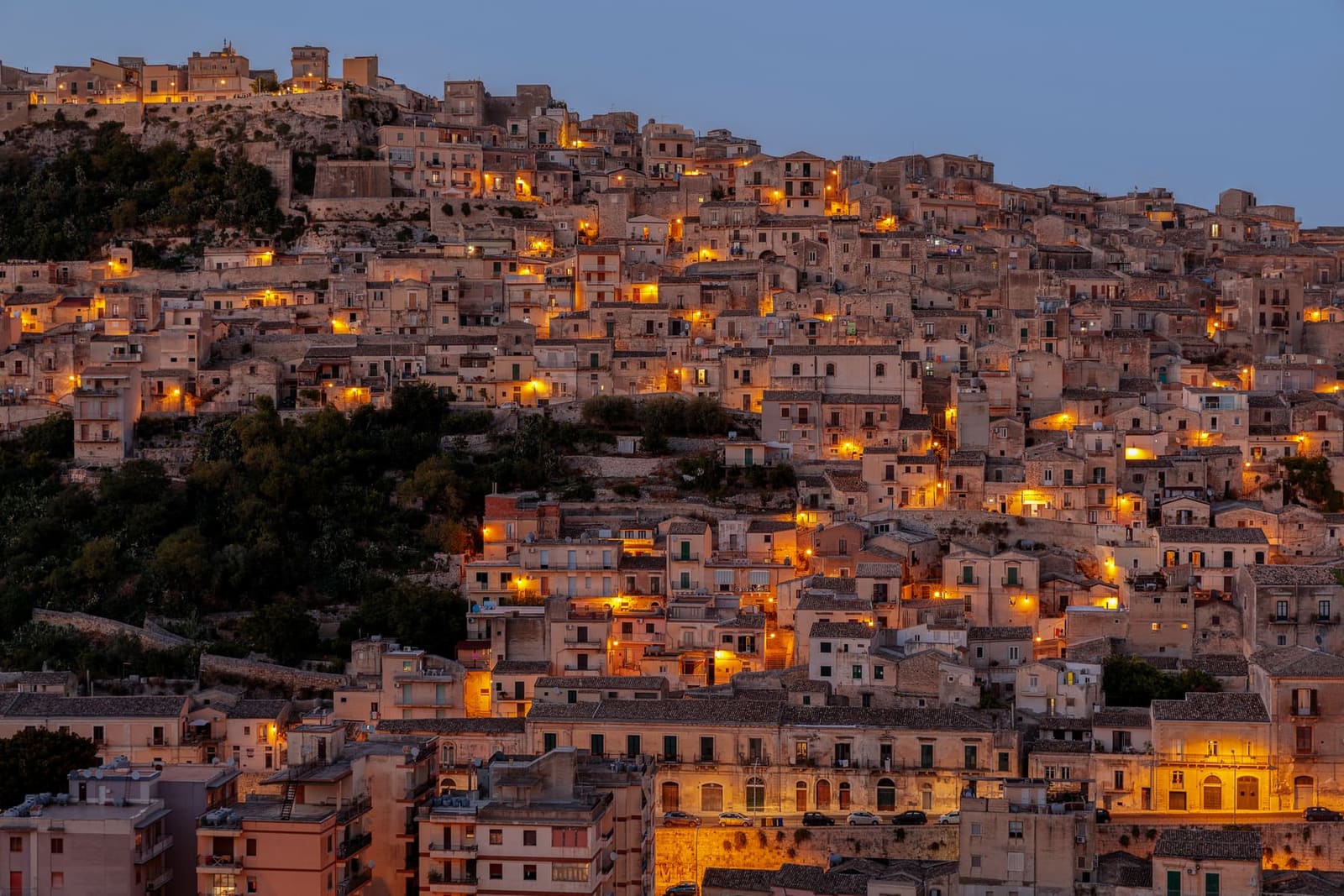 le case di Modica una sopra l'altra sul fianco della collina, con le luci che si accendono all'imbrunire