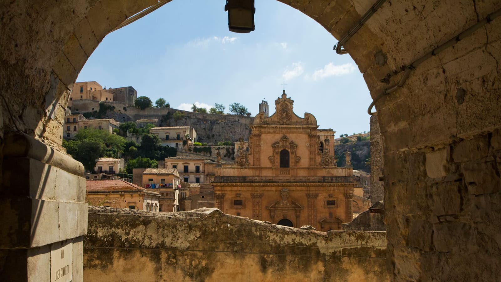 il Duomo di San Pietro visto da sotto un arco, con le case di Modica Alta sulla collina dietro