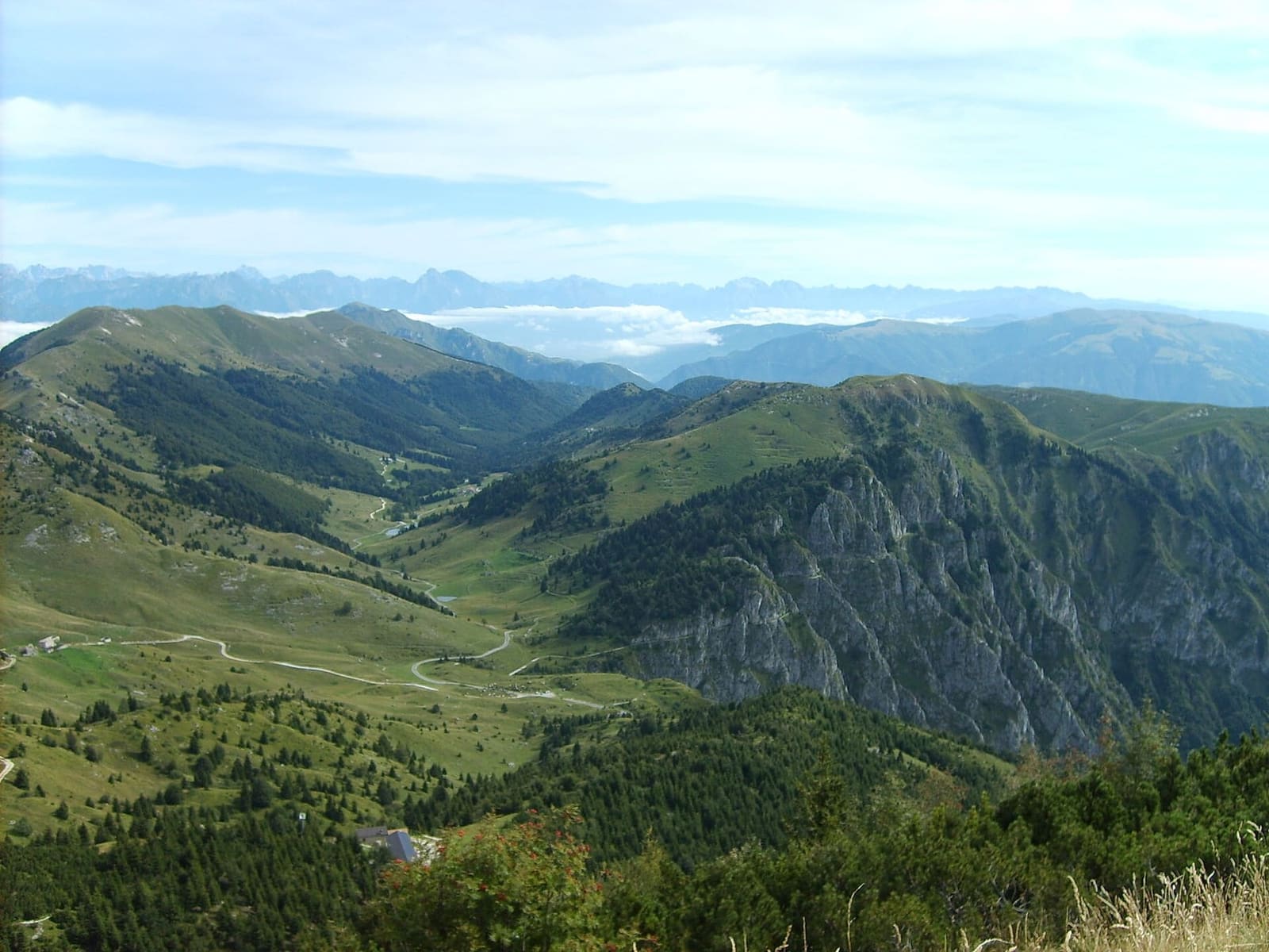 dalla cima verso nord, i pascoli e le valli del massiccio con le Dolomiti all'orizzonte, ad agosto