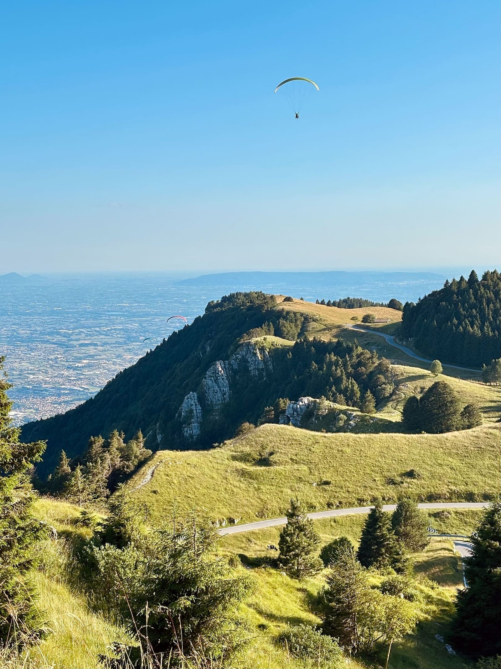 un parapendio sopra i prati del Grappa, con la pianura veneta sotto, in una sera di luglio