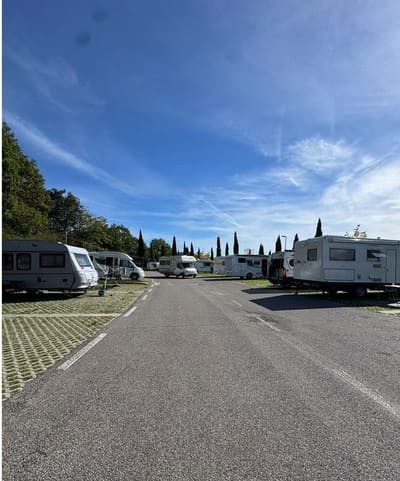 i camper e le roulotte in fila sulle piazzole dell'area di sosta, fra i cipressi